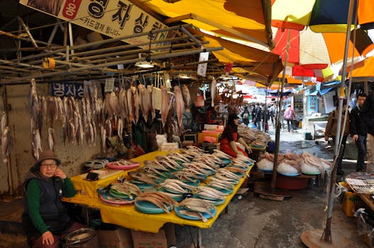 Lively Asian fish market scene with fresh seafood and colorful umbrellas, bustling with people.