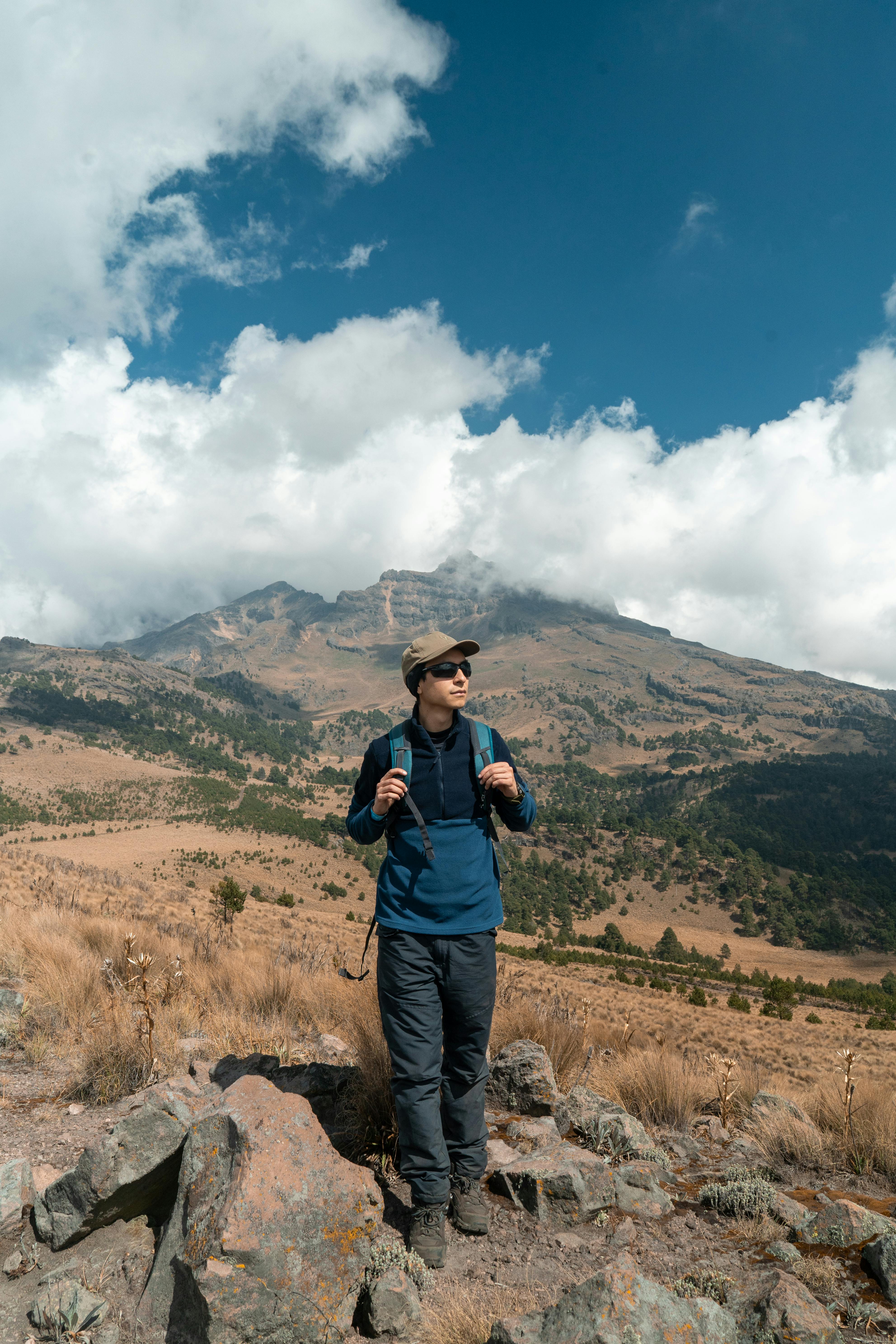 Kostenlos Abenteuersuchender wandert durch unwegsames Gebirgsgelände unter Wolken. Stock-Foto