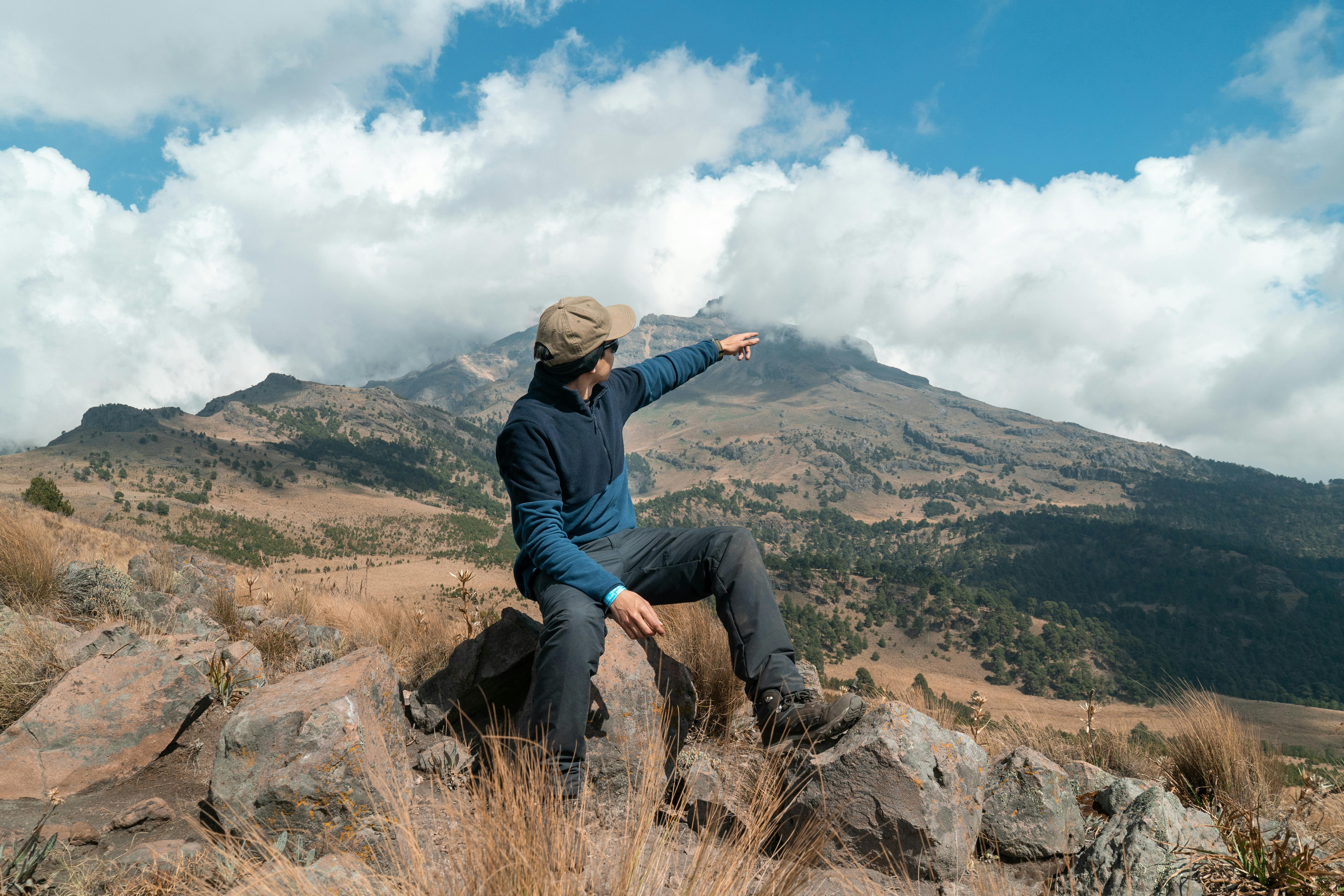 Gratuit Bărbat arătând spre un teren muntos pitoresc. Cerul senin și mediul stâncos creează un sentiment de aventură. Fotografie de stoc