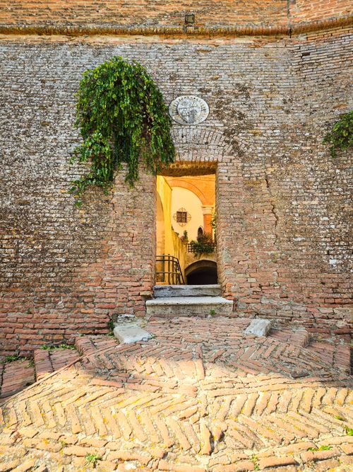 Free Old brick archway with ivy leading to a sunlit courtyard in a historical building. Stock Photo