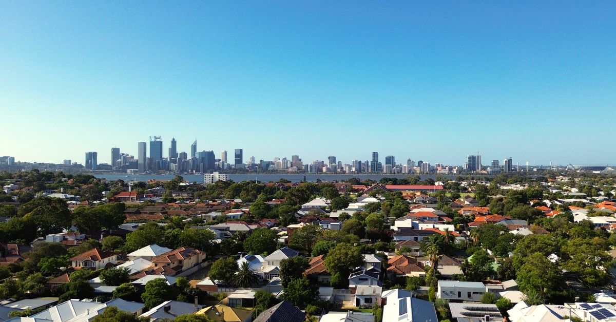 Stunning aerial view of Perth city skyline and suburban homes under clear blue sky.
