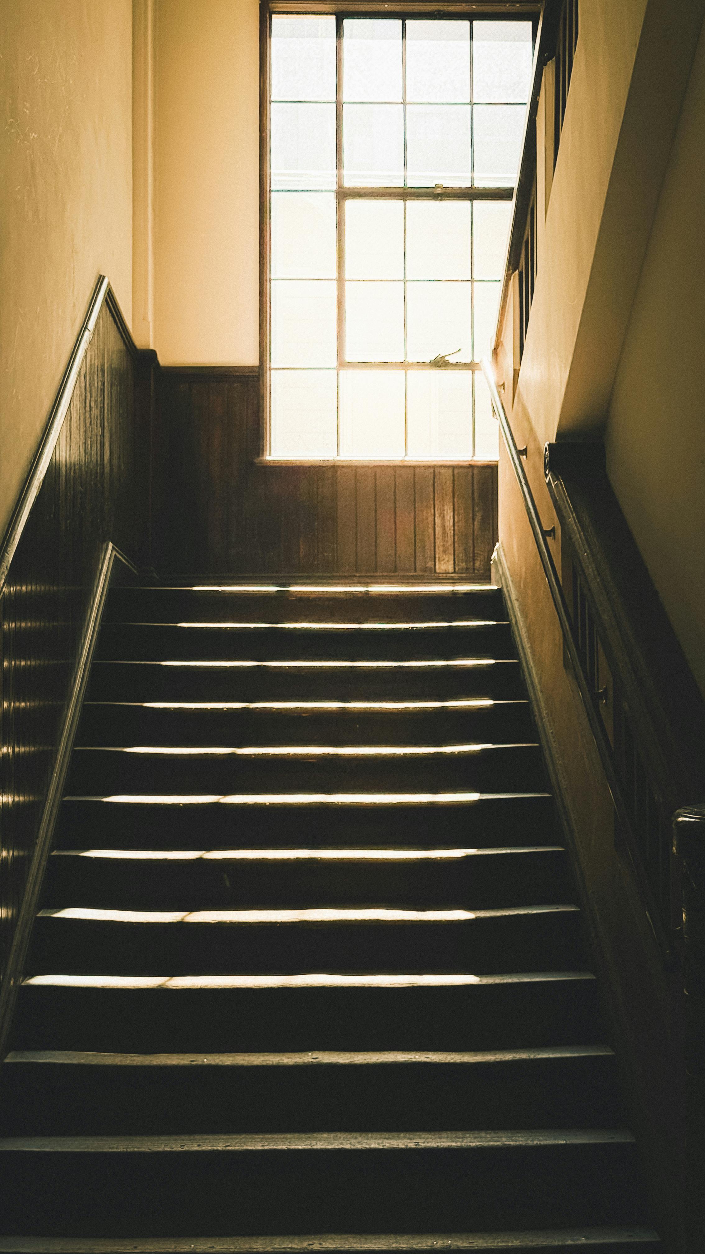 Δωρεάν Μια vintage σκάλα με το φως του ήλιου να ρέει μέσα από ένα μεγάλο παράθυρο, δημιουργώντας ένα εντυπωσιακό εφέ. Φωτογραφία από στοκ φωτογραφιών