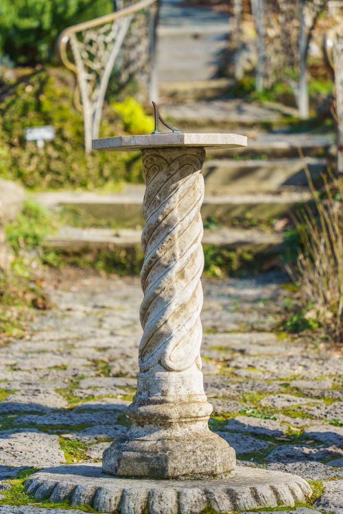 Free A classic sundial on a spiral stone pedestal amidst a sunny garden setting. Stock Photo