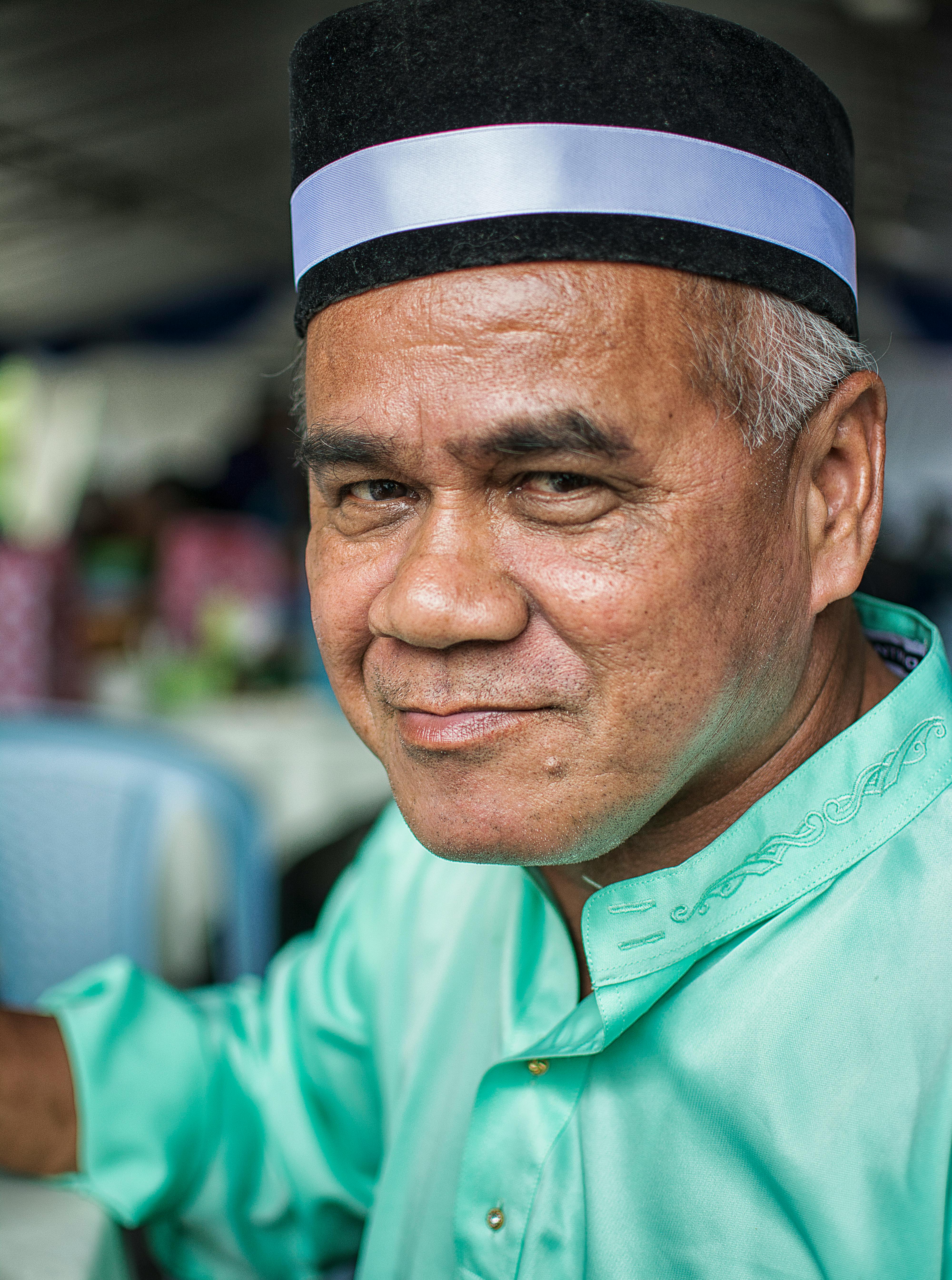 Kostenlos Ein älterer Mann in traditioneller schwarz-weißer Mütze und grüner Kleidung lächelt im Freien. Stock-Foto