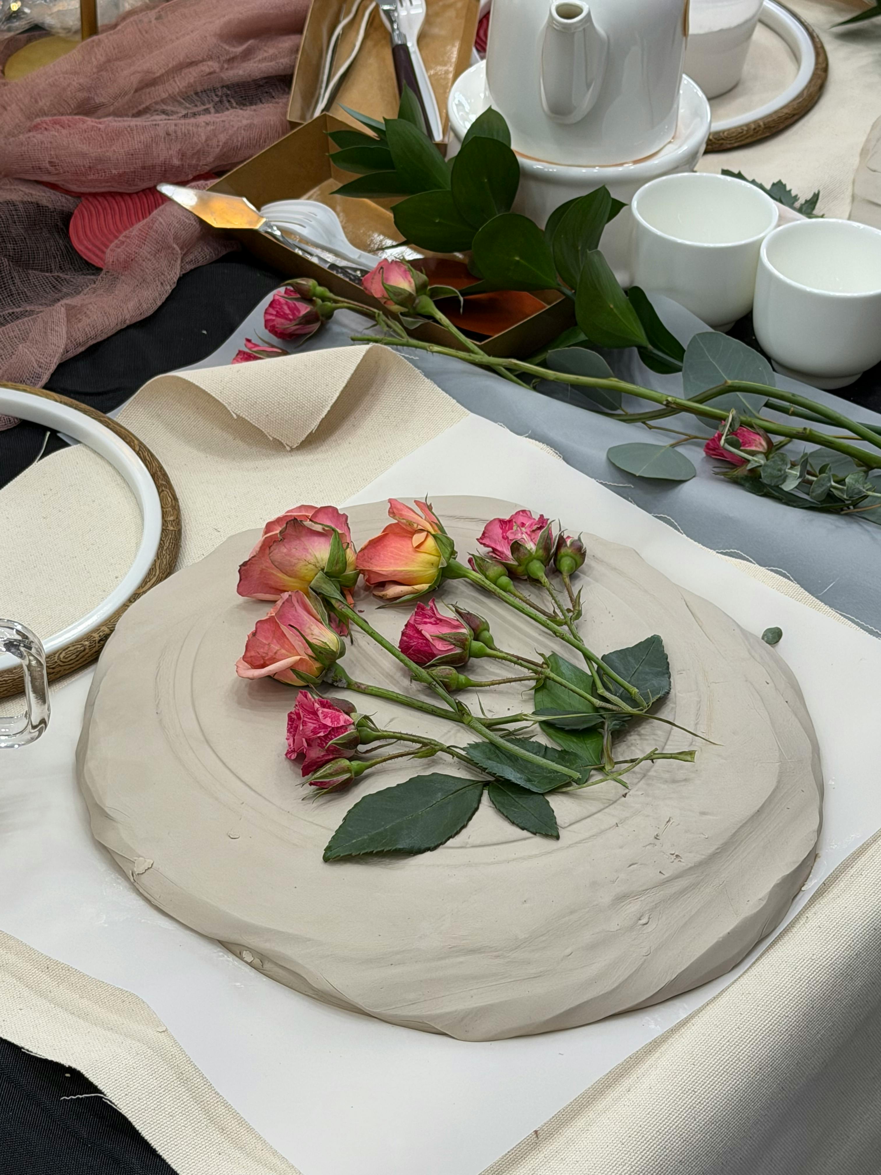 Kostenlos Elegante Rosenanordnung auf einem Keramikteller, umgeben von einem Teeservice und Stoff. Stock-Foto