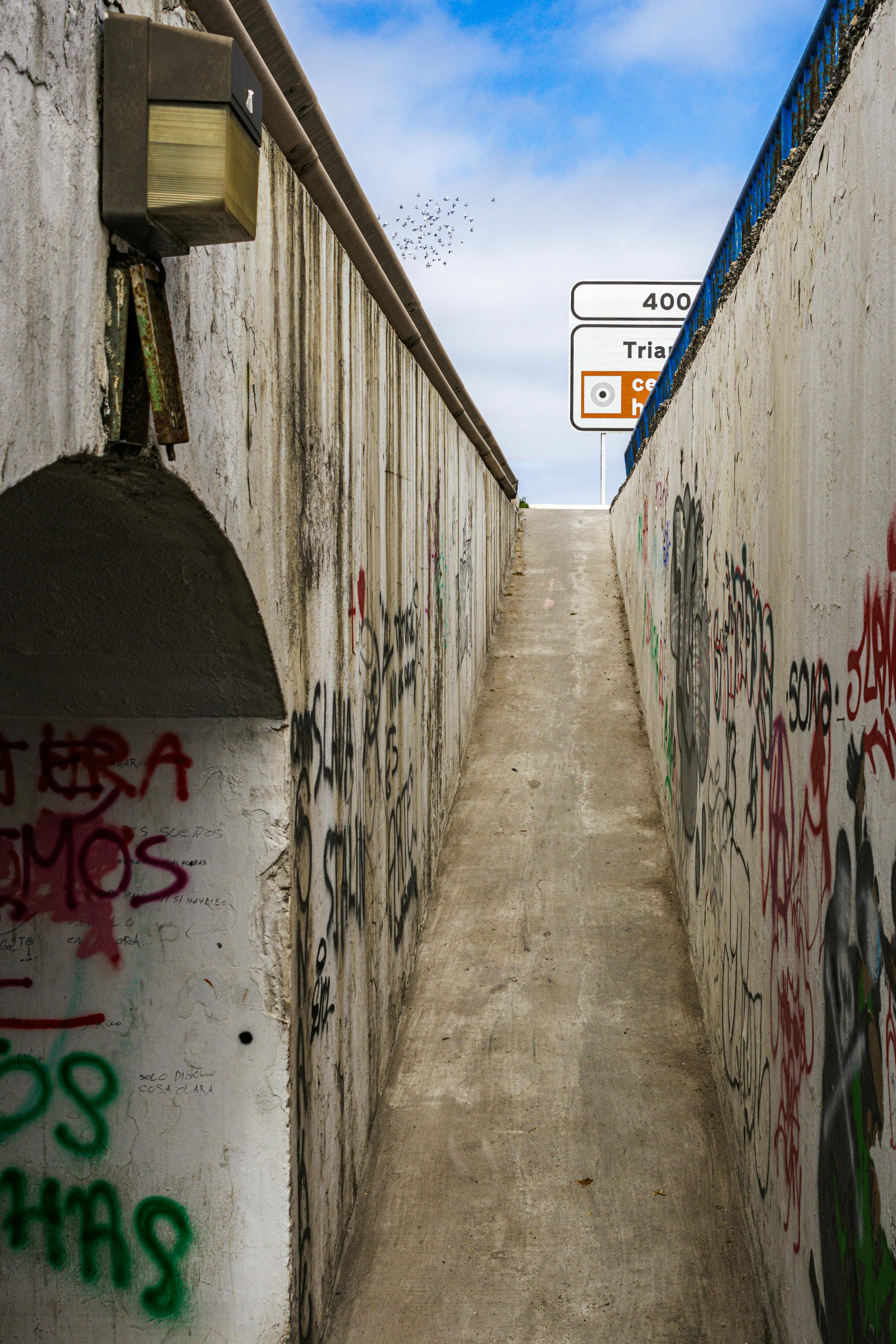 Δωρεάν Στενό σοκάκι ανάμεσα σε τσιμεντένιους τοίχους καλυμμένους με γκράφιτι, που οδηγεί στις πινακίδες οδικής κυκλοφορίας από πάνω. Φωτογραφία από στοκ φωτογραφιών