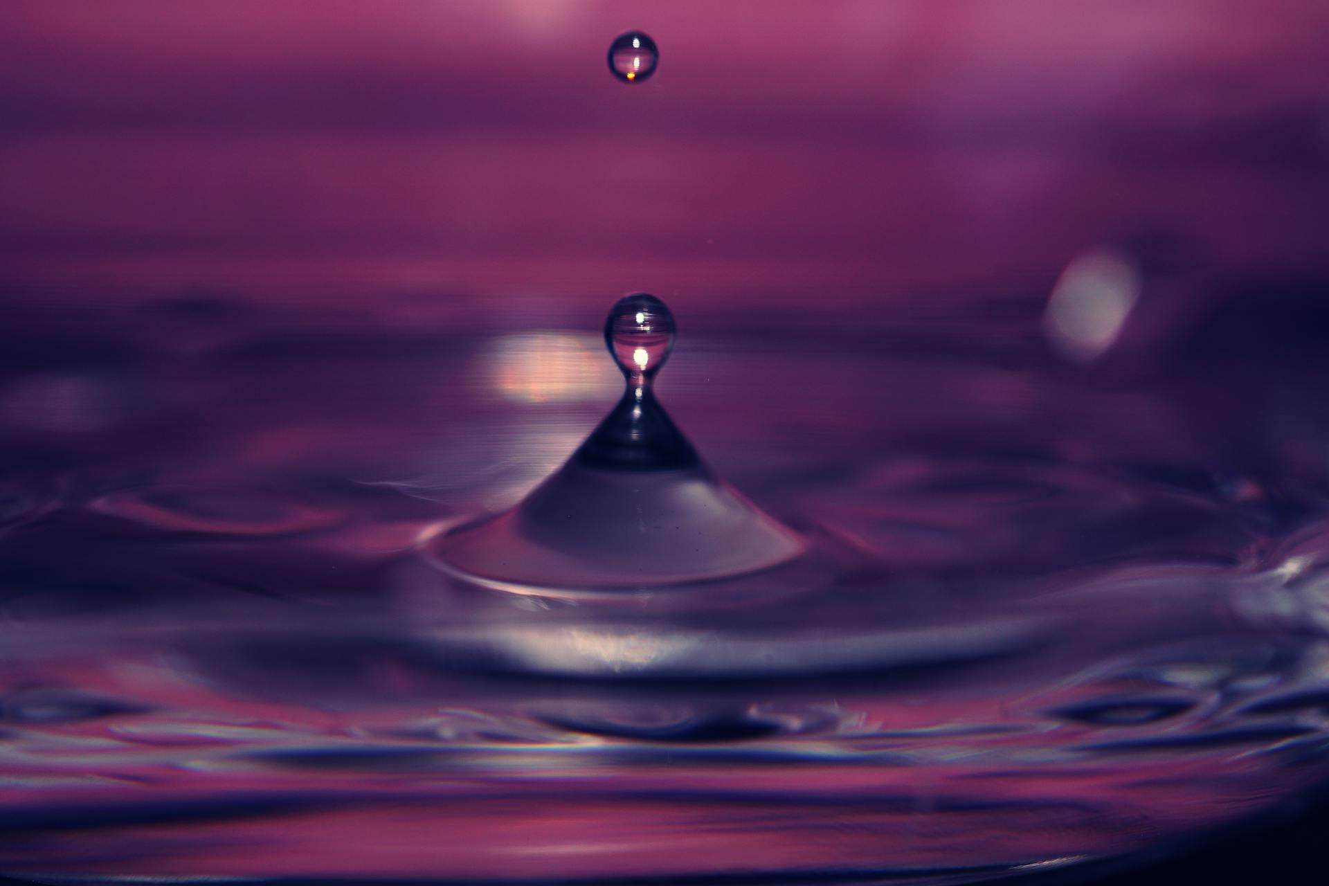 Captivating close-up of a water droplet creating ripples against a vivid purple backdrop.