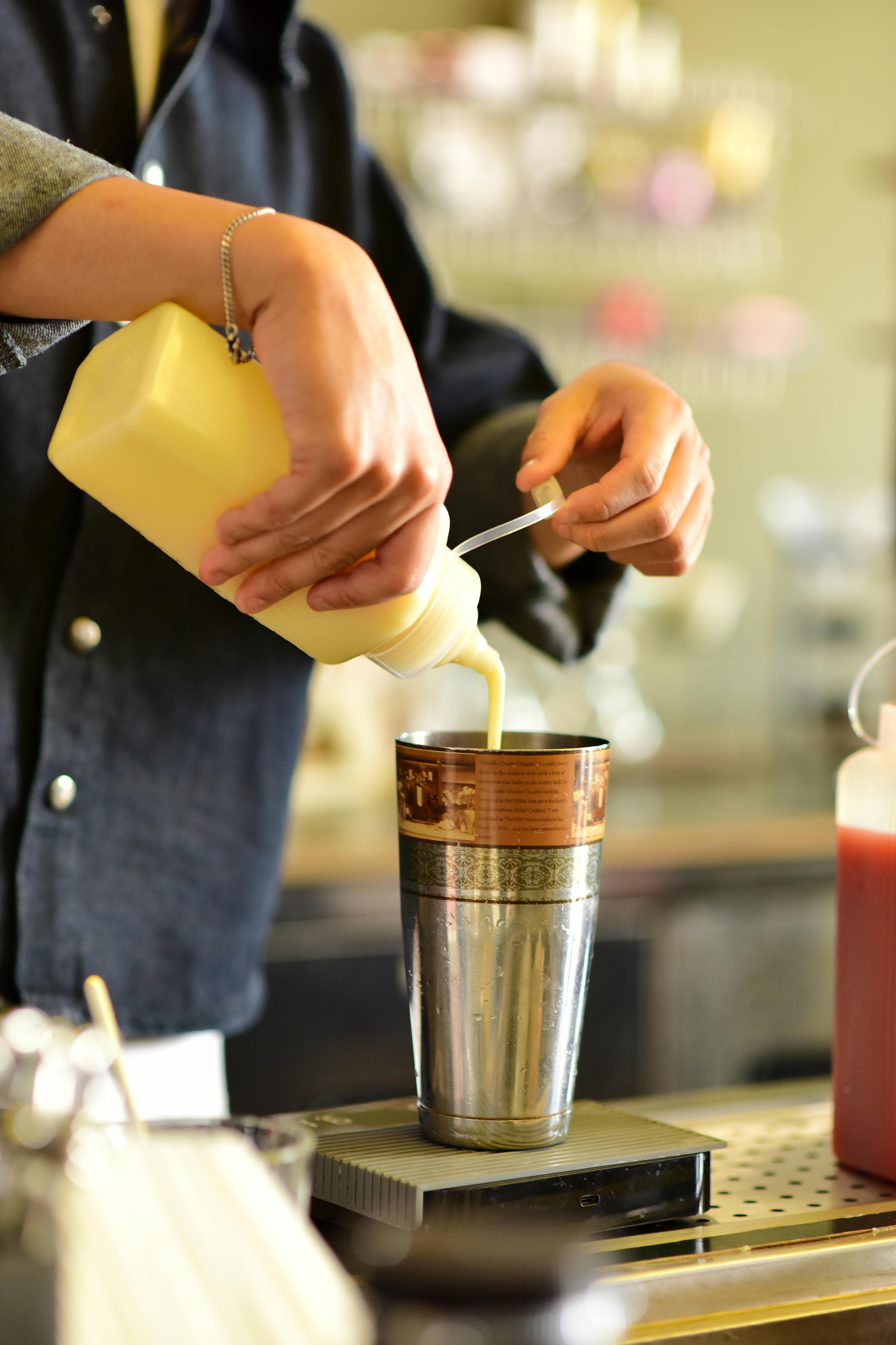 Kostenlos Ein Barista gießt gekonnt eine cremige Mischung in einen Shaker an der Theke eines Cafés. Stock-Foto
