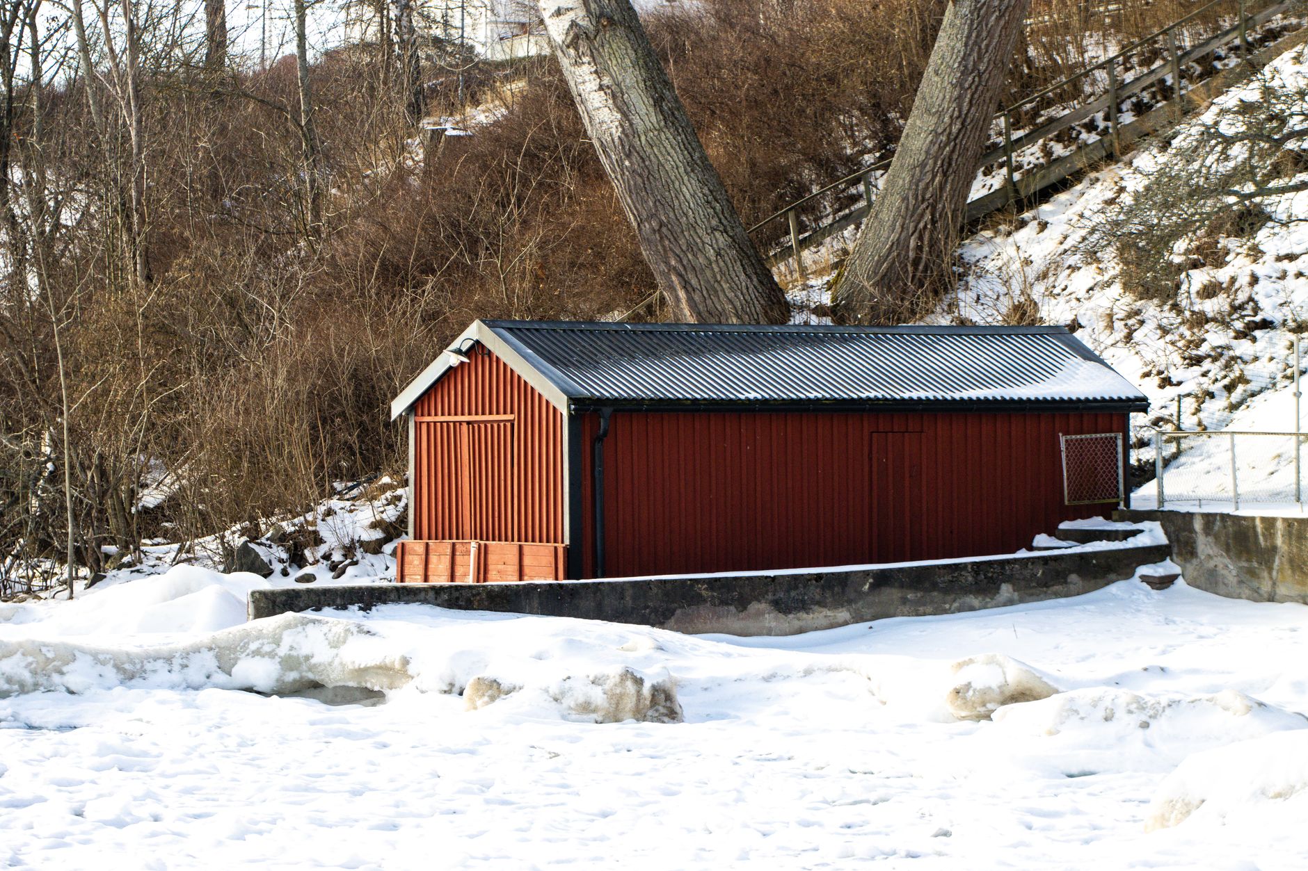 A red wooden shed surrounded by snow in a wooded area of Jönköping, Sweden.