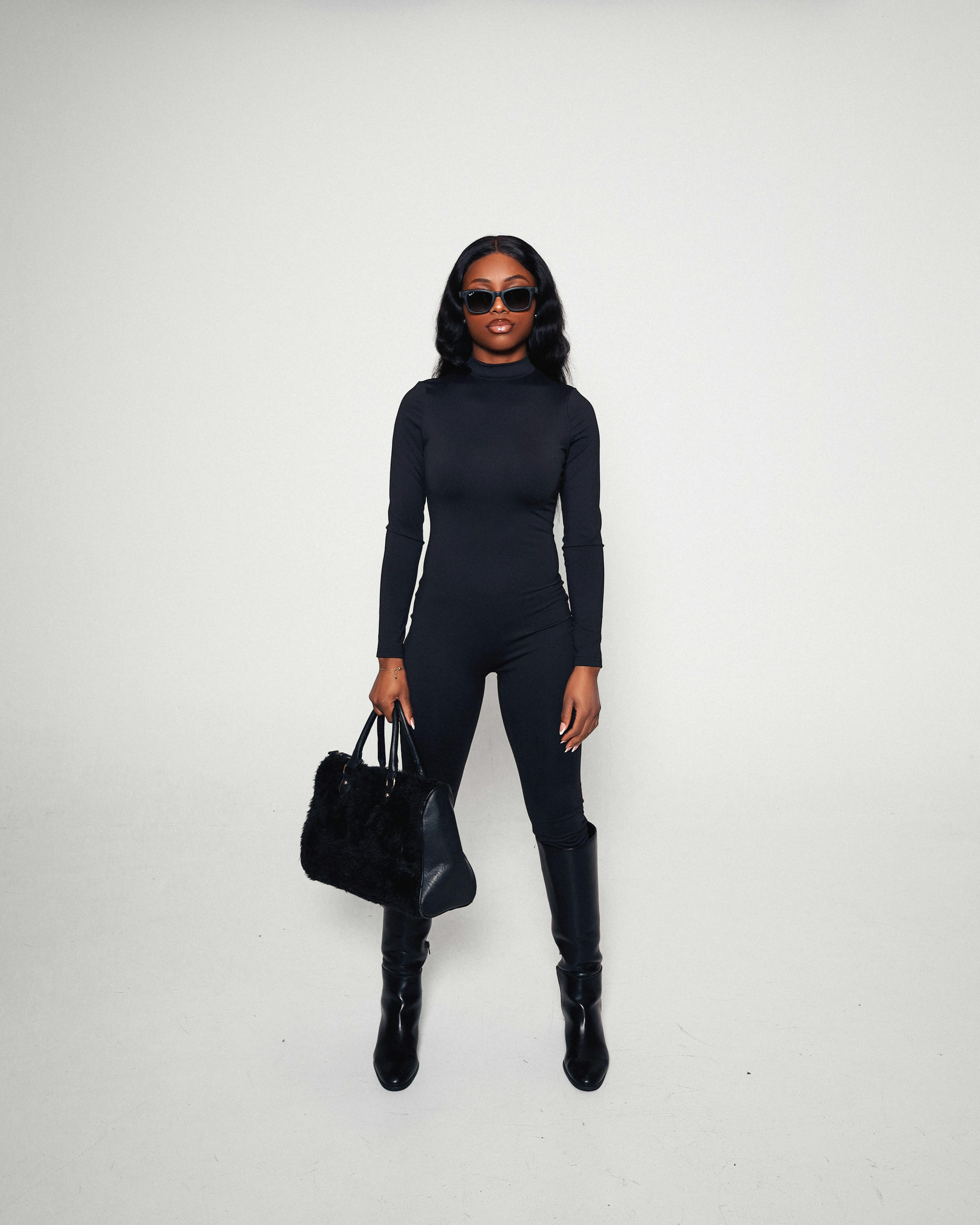 Δωρεάν Μοντέρνα γυναίκα με ολόσωμη μαύρη στολή που κρατά μια τσάντα χειρός, αποπνέοντας μοντέρνα κομψότητα. Φωτογραφία από στοκ φωτογραφιών