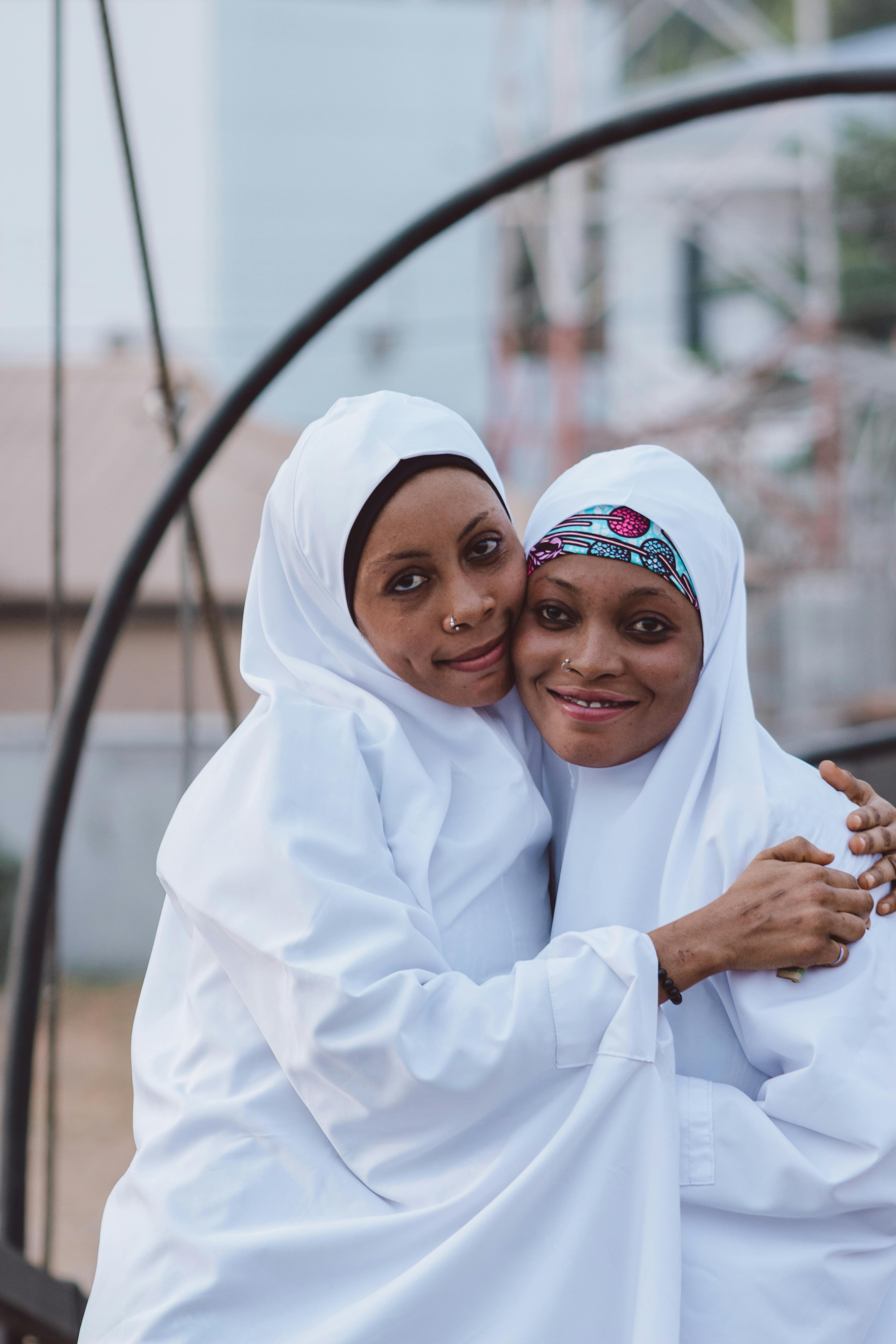 Kostenlos Zwei Frauen in weißen Hijabs umarmen sich im Freien mit freudigem Ausdruck. Stock-Foto