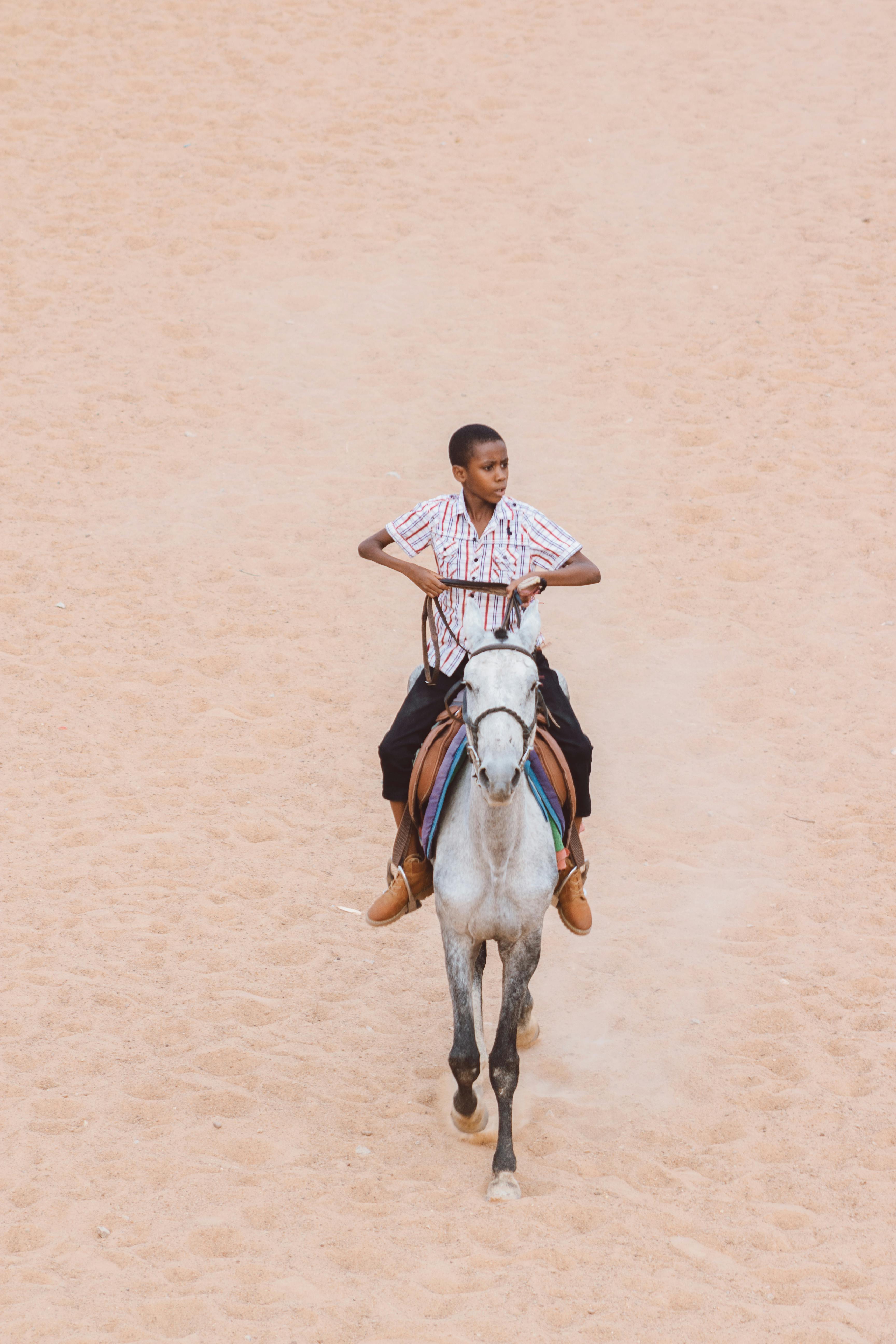 Kostenlos Ein junger Mann reitet souverän auf einem Pferd durch ein weites Sandgebiet und fängt so einen Moment gekonnter Reitkunst ein. Stock-Foto