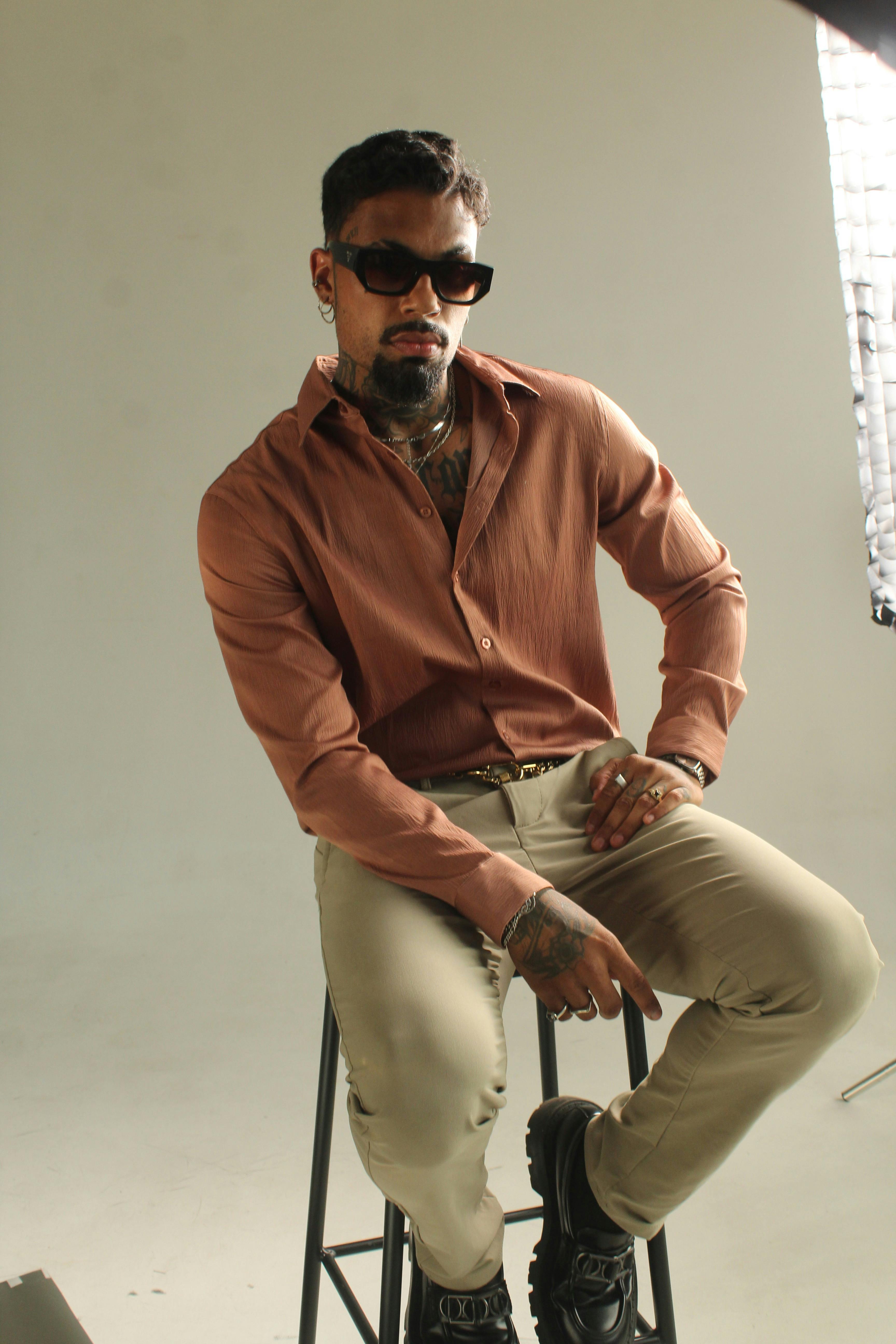 Free Portrait of a man with tattoos wearing sunglasses and casual attire seated indoors. Stock Photo