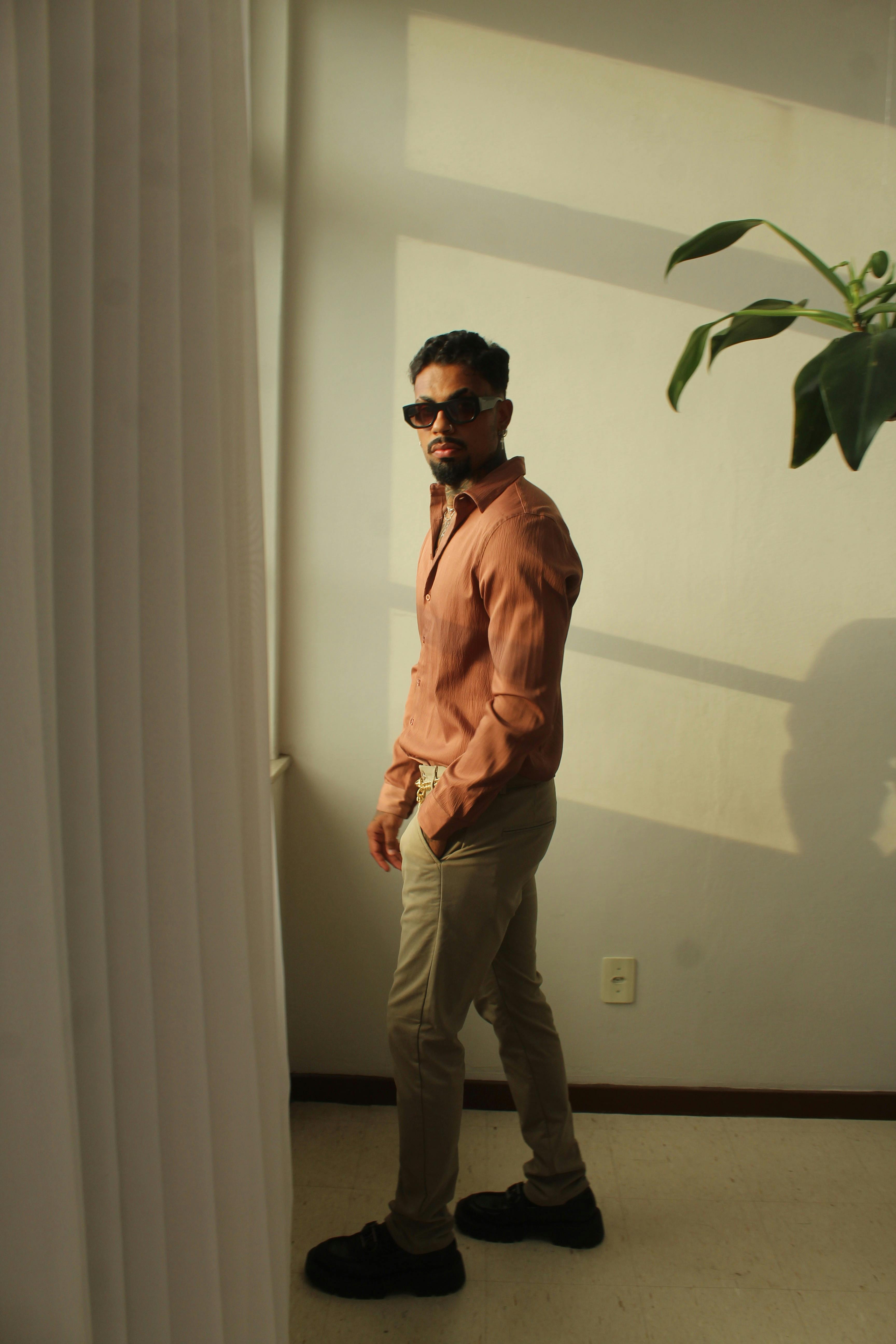 Δωρεάν Άνδρας που φοράει γυαλιά ηλίου και στέκεται δίπλα σε ένα ηλιόλουστο παράθυρο με φυτική διακόσμηση σε εσωτερικό χώρο. Φωτογραφία από στοκ φωτογραφιών