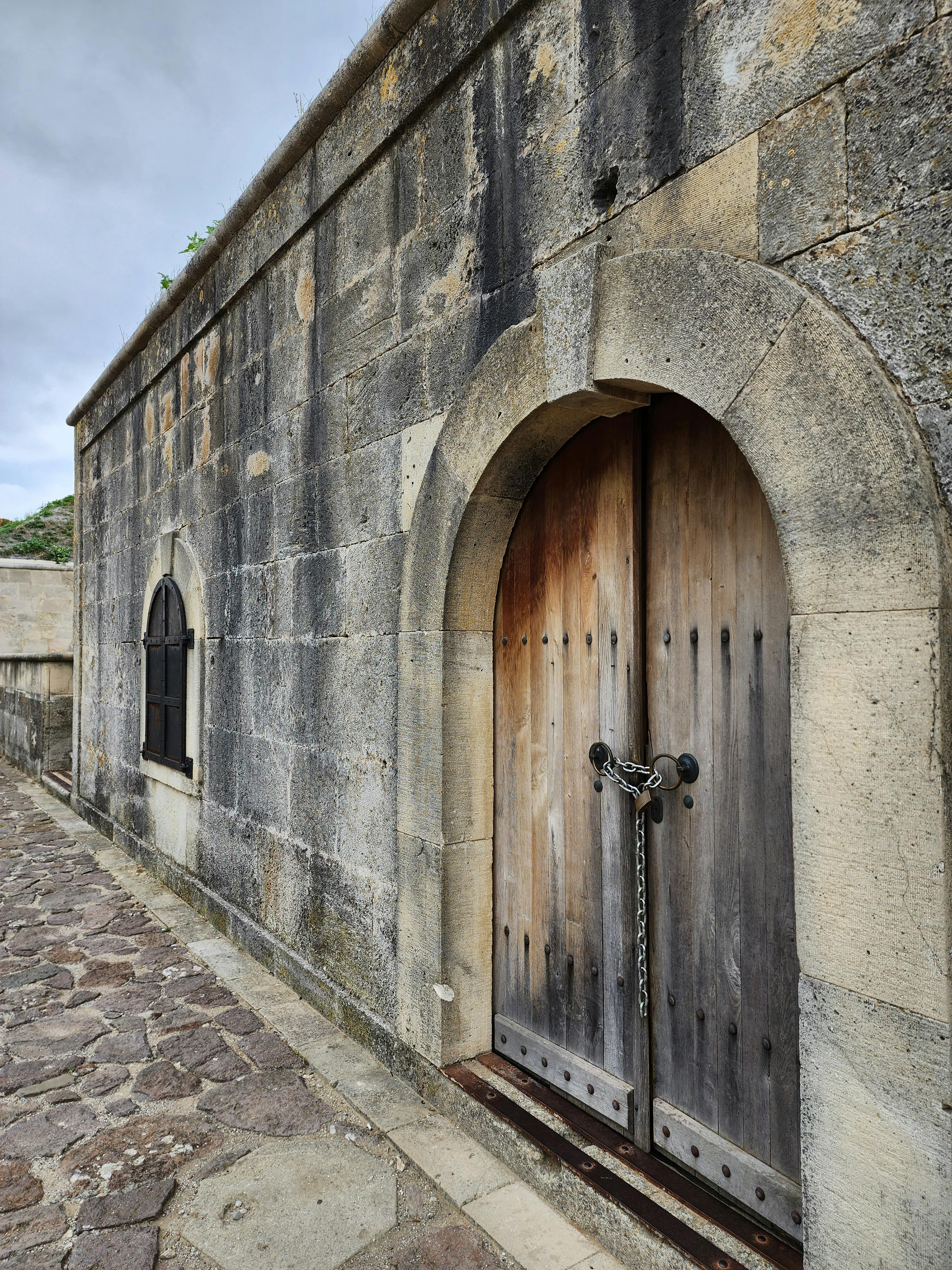 Kostenlos Rustikales Steingebäude mit gewölbter Holztür, die tagsüber mit einer Kette verschlossen ist. Stock-Foto