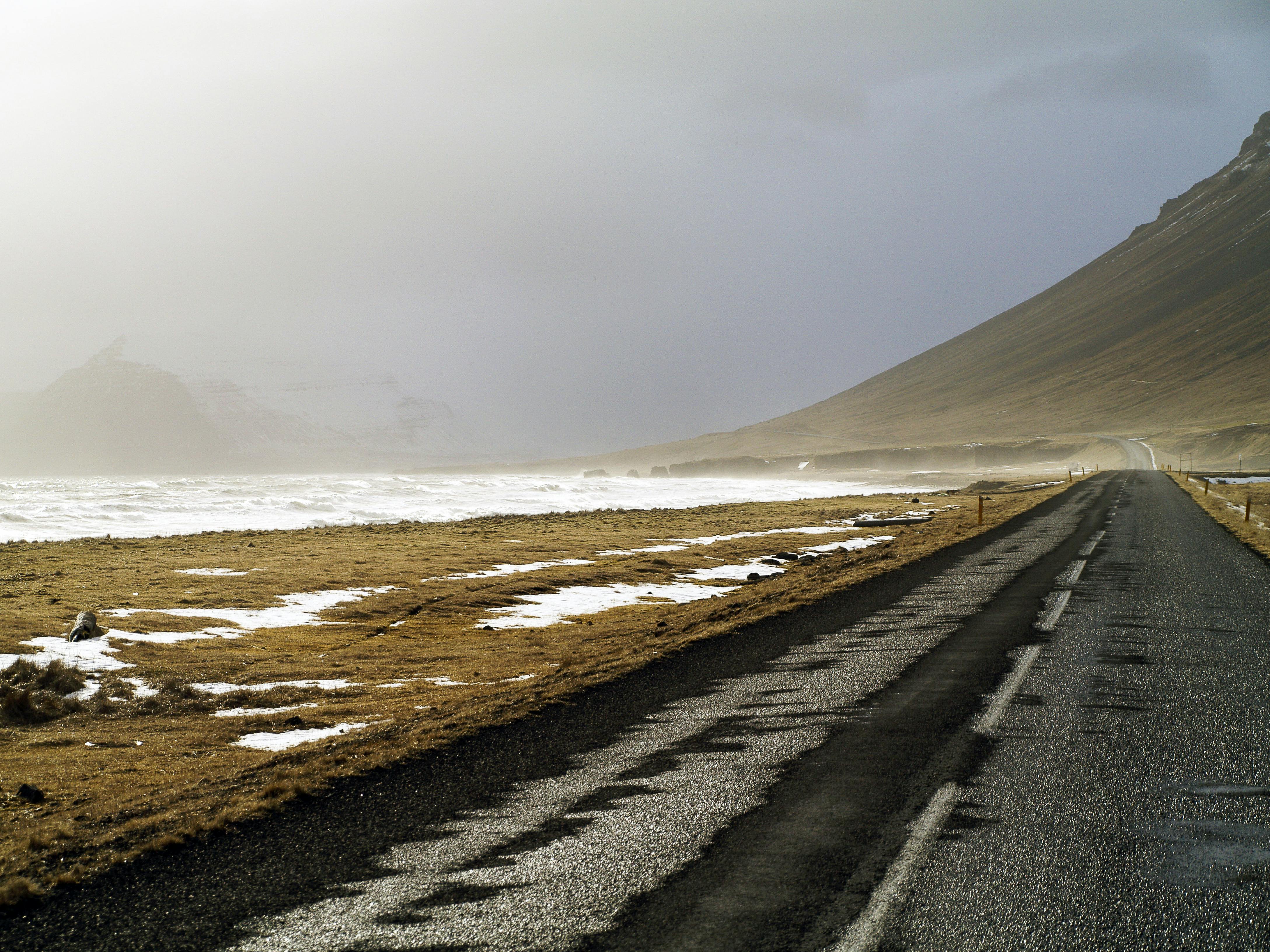 Kostenlos Eine stimmungsvolle Küstenstraße in Island mit nebelverhangenen Bergen und spärlichem Schneefall, die Einsamkeit und Abenteuerlust weckt. Stock-Foto
