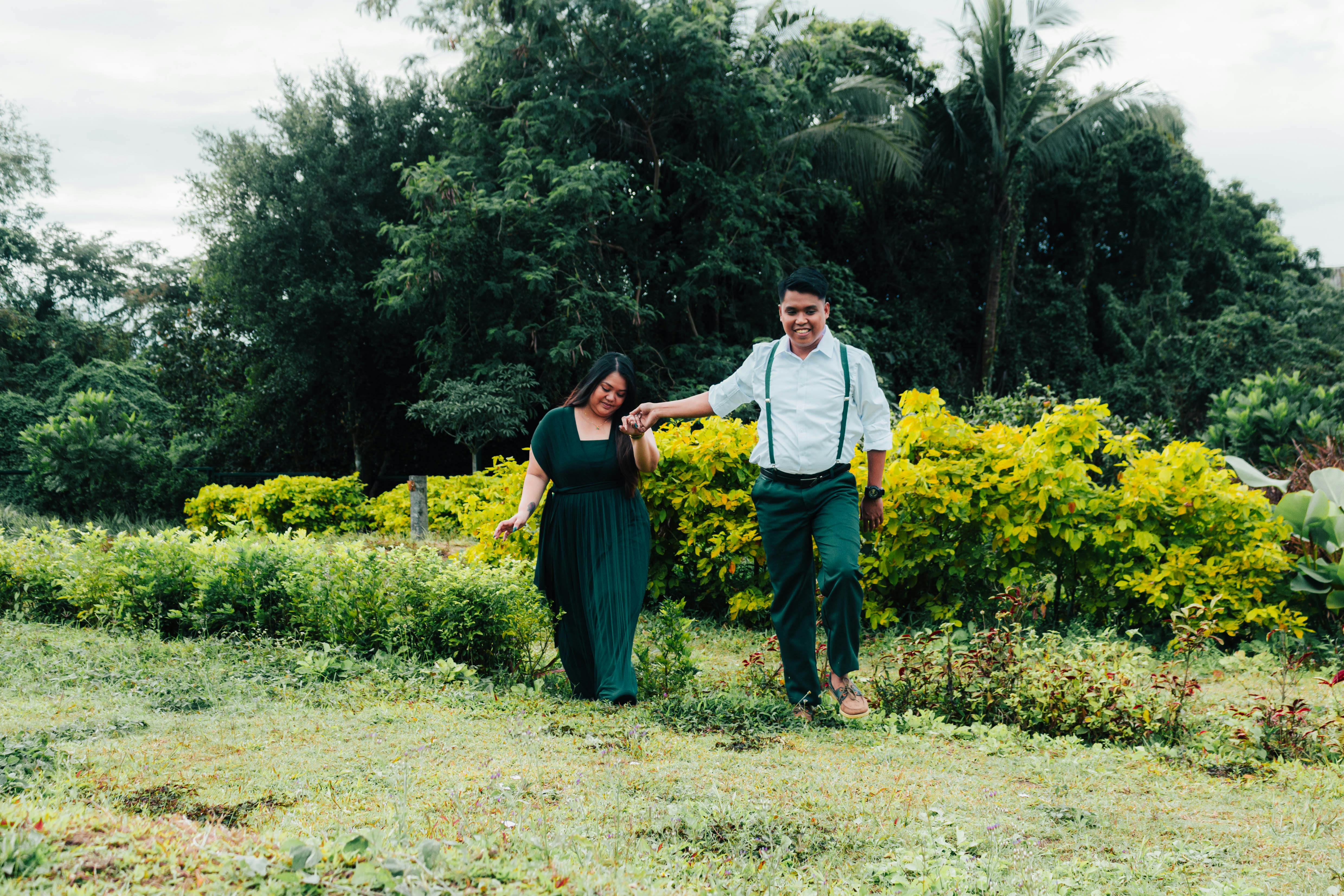 Kostenlos Ein glückliches Paar spaziert Hand in Hand durch einen üppig grünen Garten an einem sonnigen Tag Stock-Foto