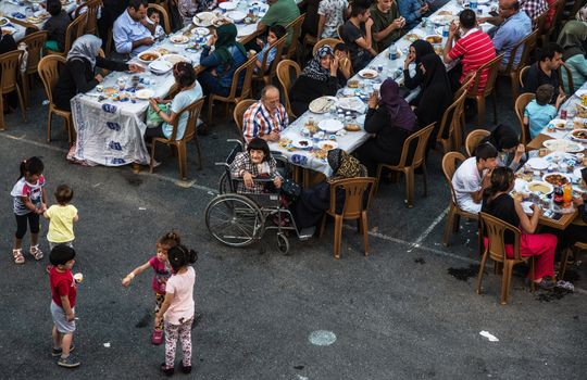 An outdoor communal dinner with people of various ages and backgrounds enjoying a meal together.
