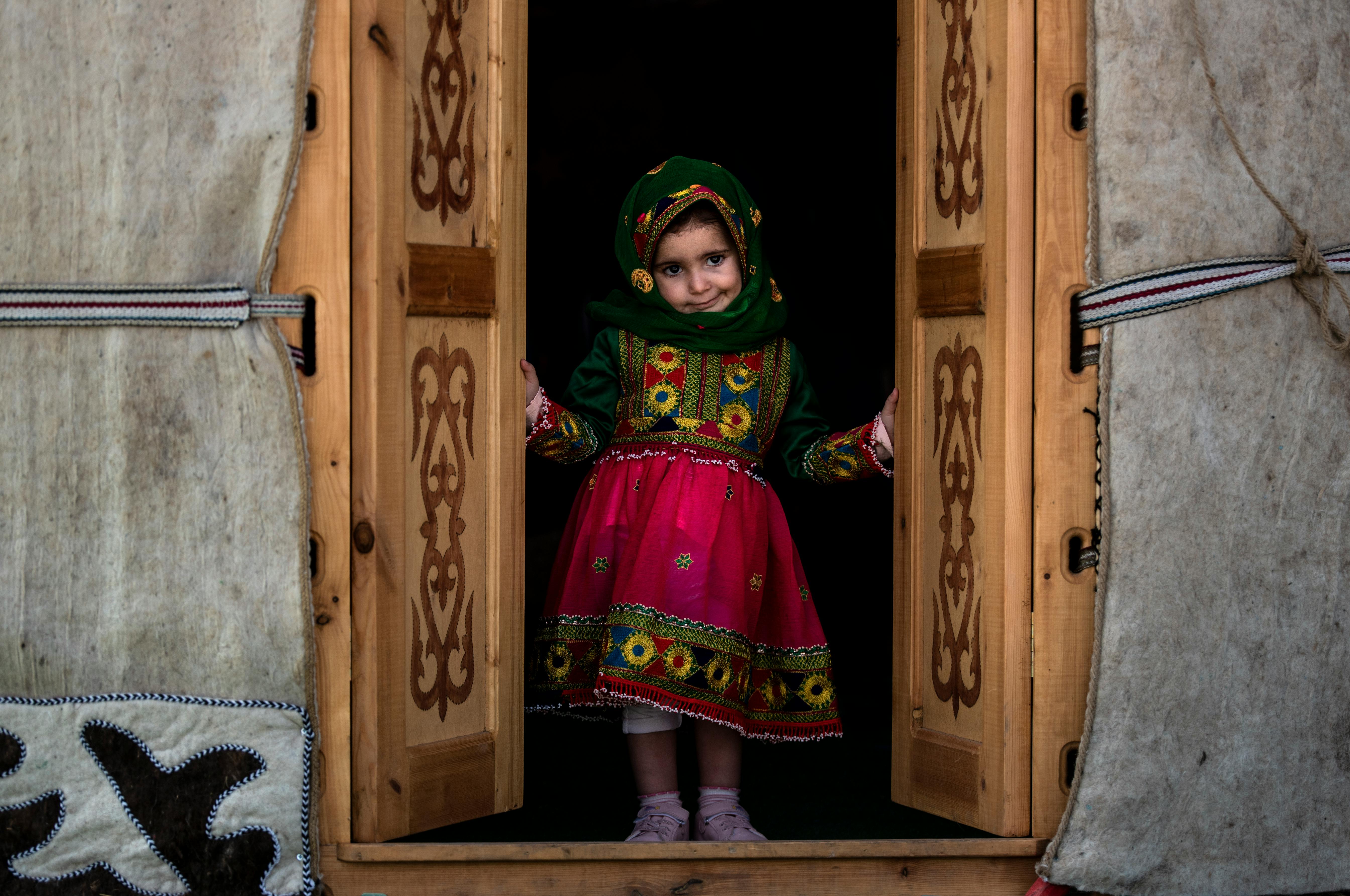 Kostenlos Ein junges Mädchen steht in einem hölzernen Türrahmen und trägt farbenfrohe traditionelle Kleidung, die das kulturelle Erbe präsentiert. Stock-Foto