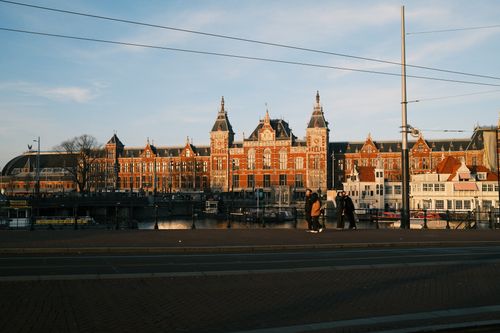 Free Captivating sunset view of the historic Amsterdam Centraal Station facade by the canal. Stock Photo