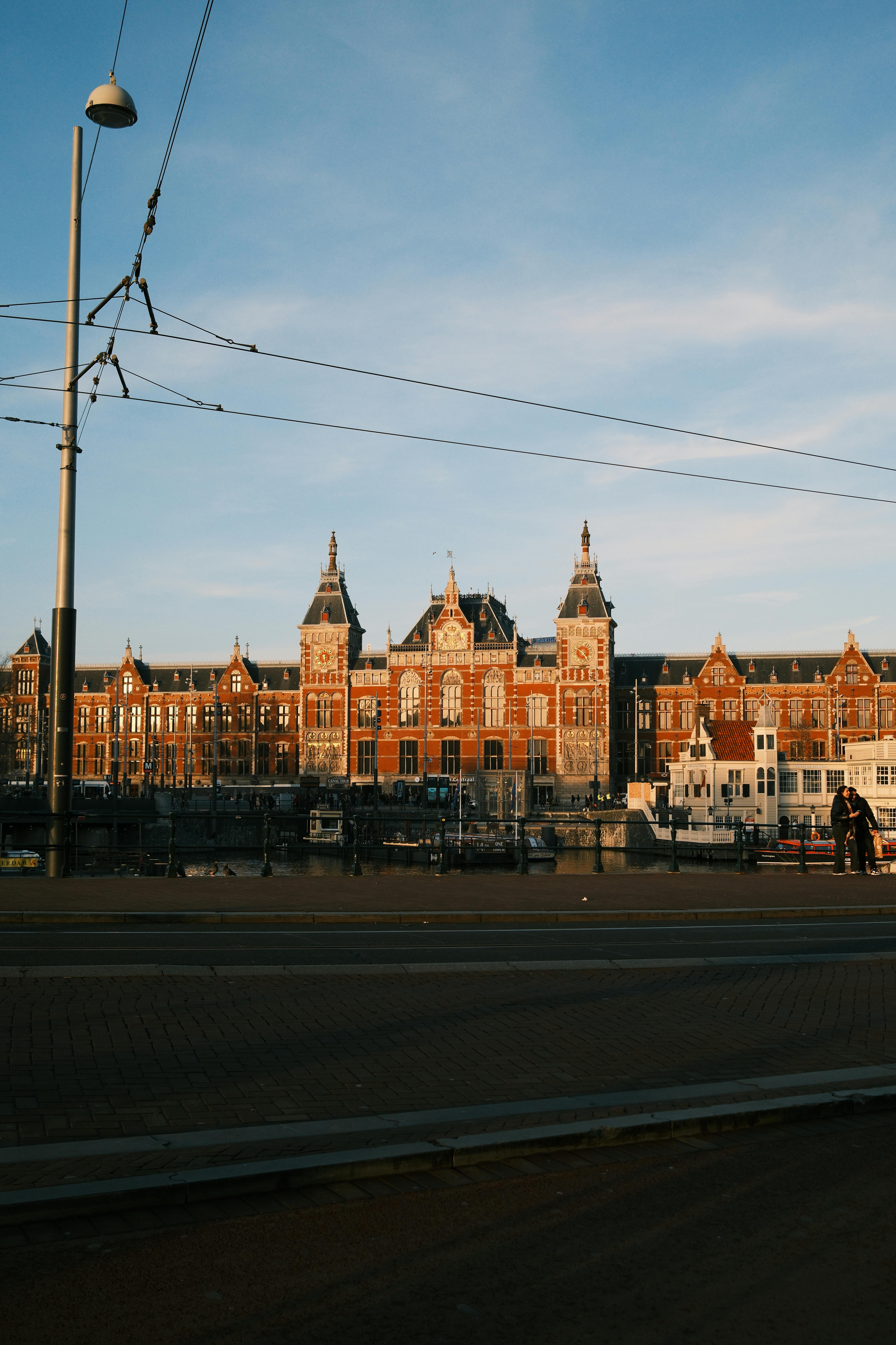 бесплатная Прекрасный закат над историческим Центральным вокзалом Амстердама, запечатлевший архитектурное великолепие. Стоковое фото