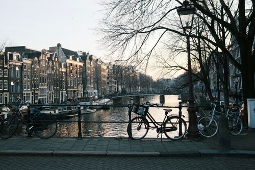 Free Amsterdam canal view with bicycles and historic buildings at twilight, capturing serene urban beauty. Stock Photo