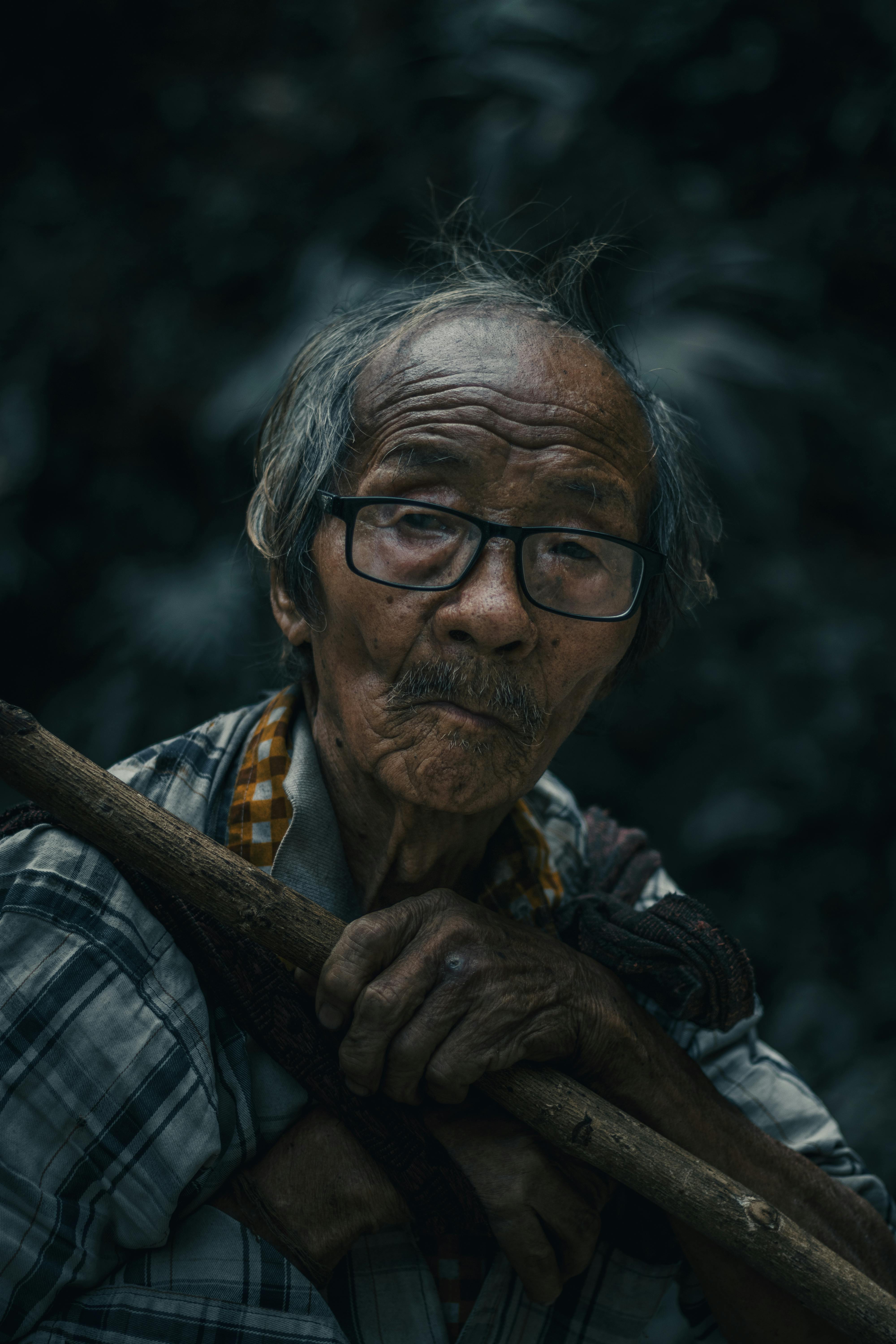 Kostenlos Porträt eines älteren Mannes mit Brille, der im Freien einen Stock hält und Weisheit und Widerstandsfähigkeit ausstrahlt. Stock-Foto