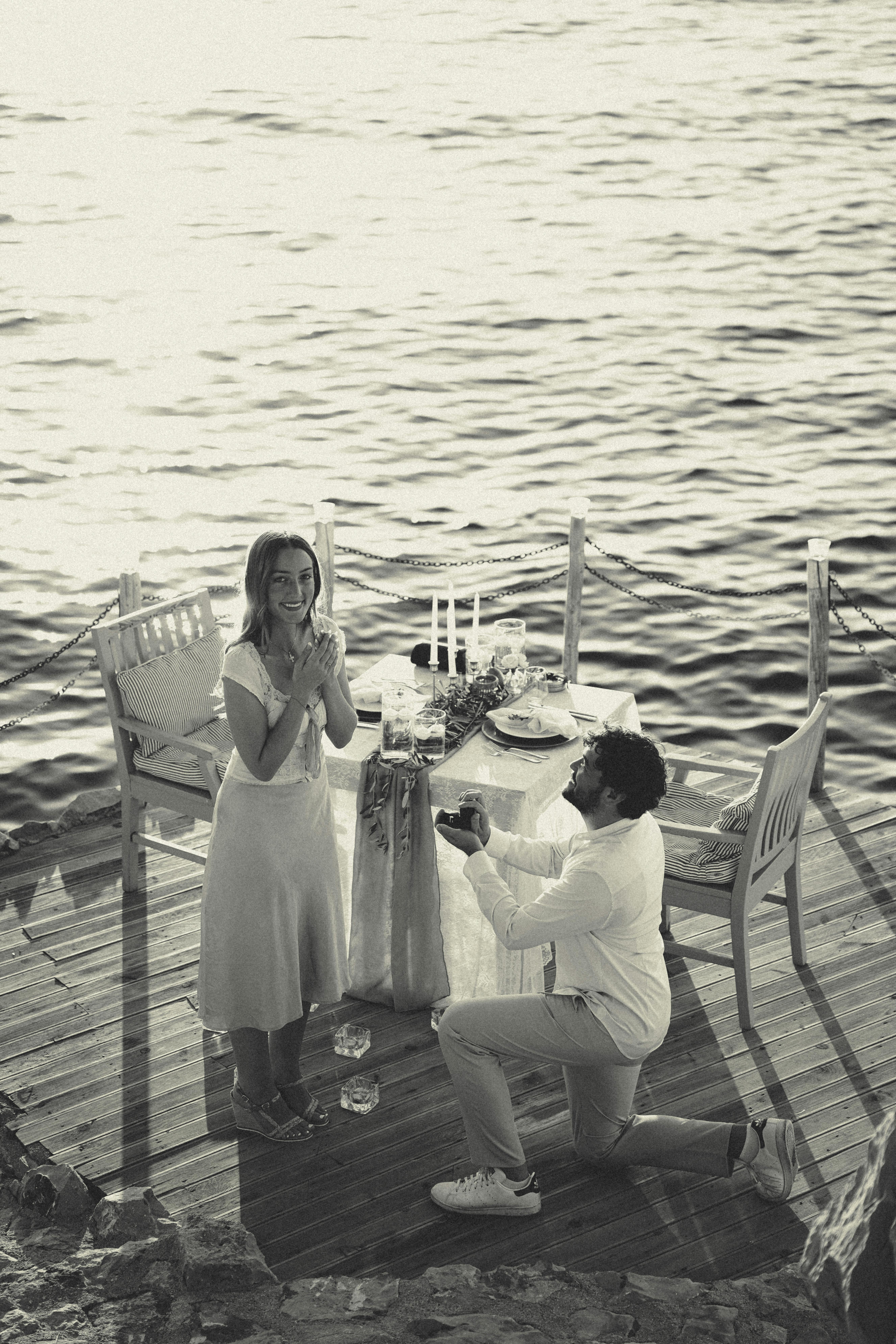 Kostenlos Ein romantischer Heiratsantrag am Meer bei Sonnenuntergang, der den Moment der Liebe und Überraschung einfängt. Stock-Foto