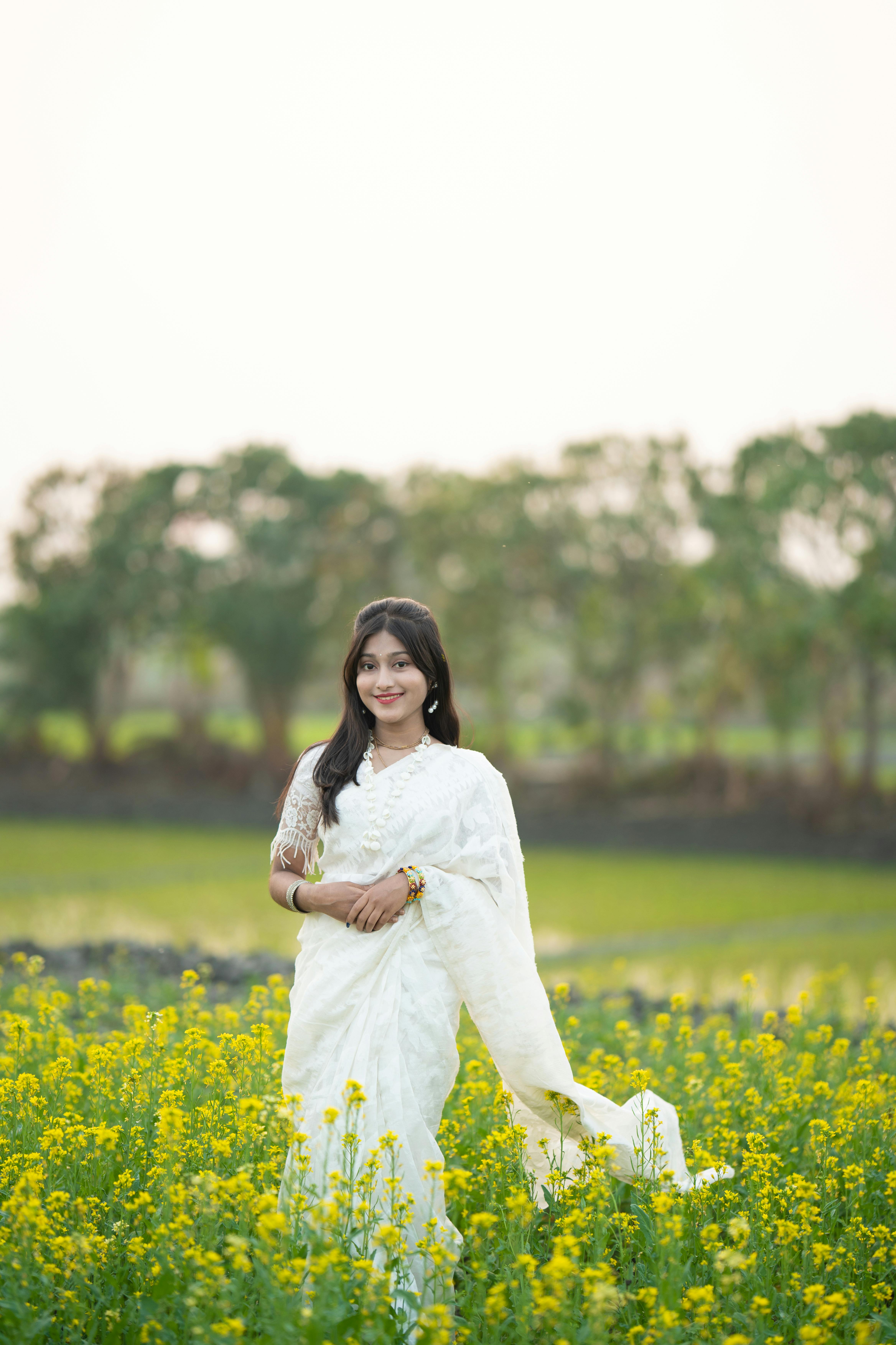 Kostenlos Eine Frau in einem weißen Sari steht anmutig in einem farbenprächtigen Blumenfeld im Tageslicht. Stock-Foto