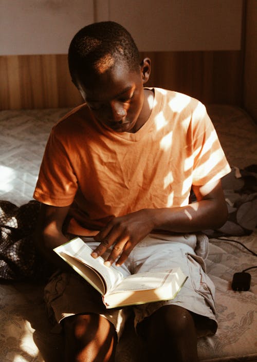 무료 책을 읽는 동안 앉아 주황색 티셔츠를 입은 소년의 사진 스톡 사진