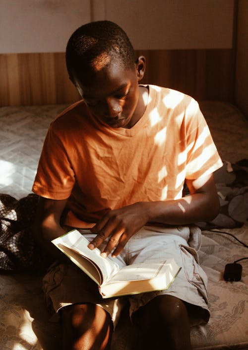 Photo of Boy Wearing an Orange T-shirt Sitting Down While Reading Book