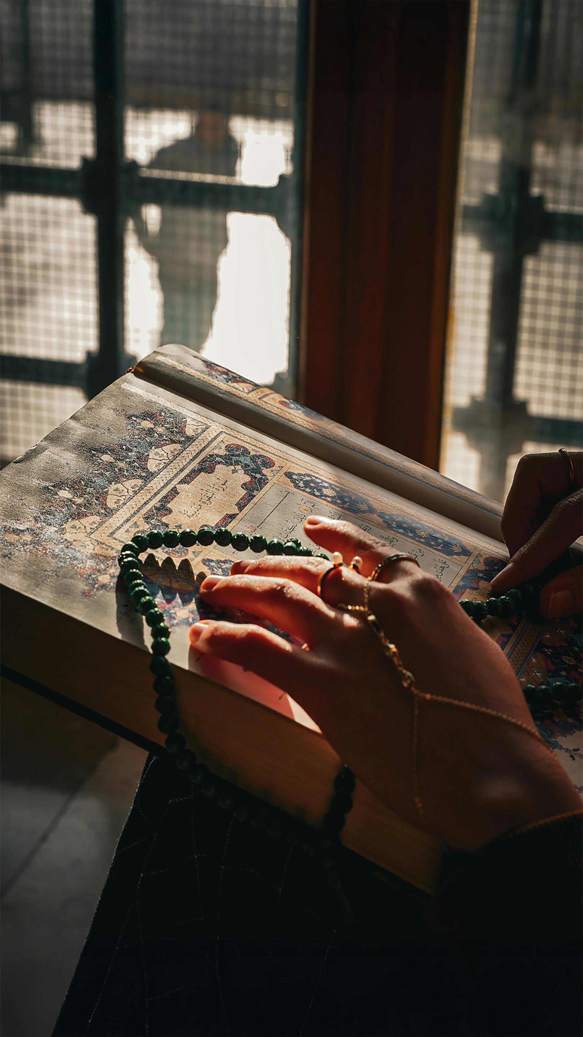 De franc Una escena serena de mans que sostenen rosaris sobre un manuscrit ornamentat en una habitació assolellada. Foto d'estoc