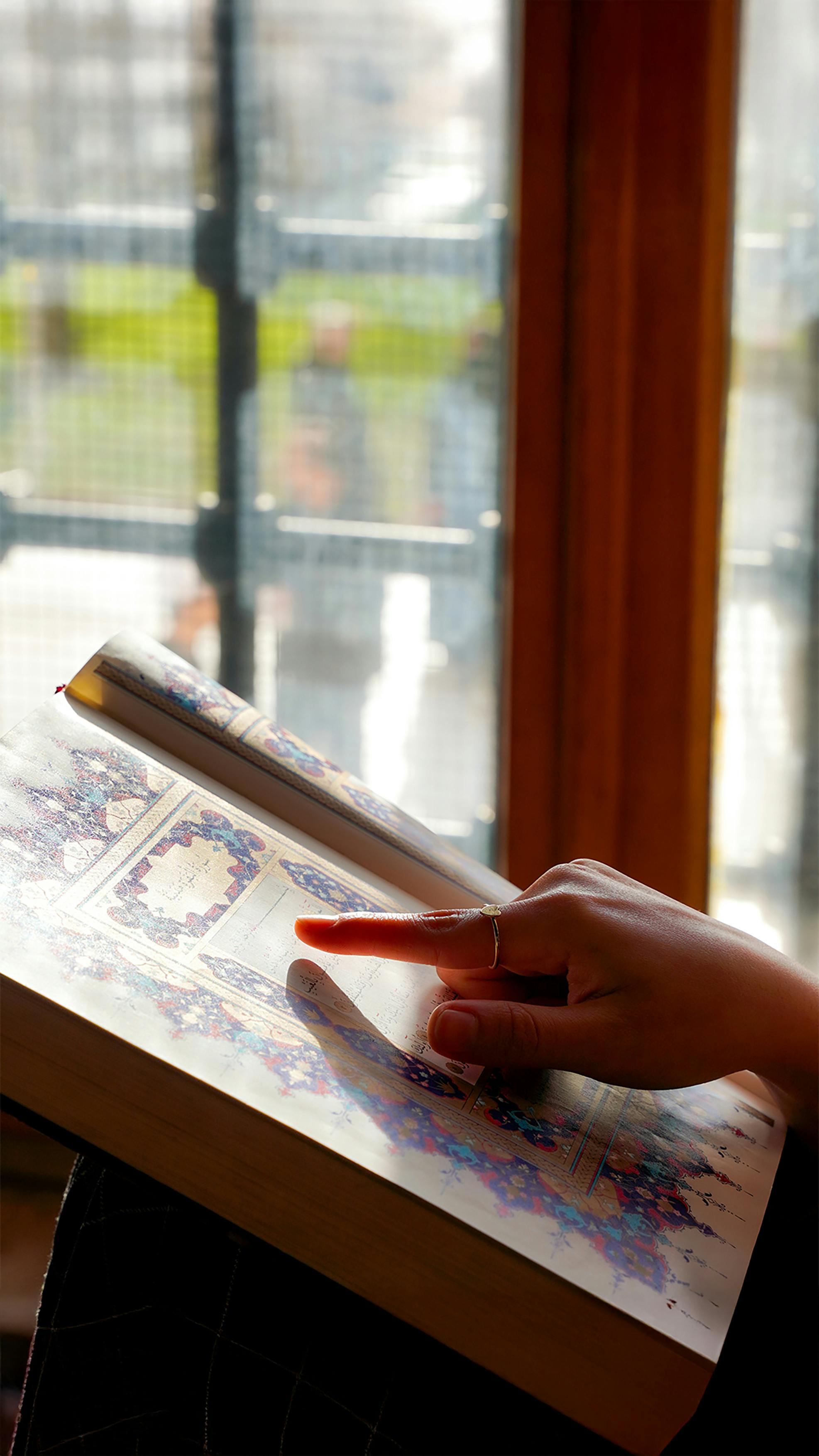 Free Hand pointing at a page in a traditional book near a sunlit window in Adana, Türkiye. Stock Photo