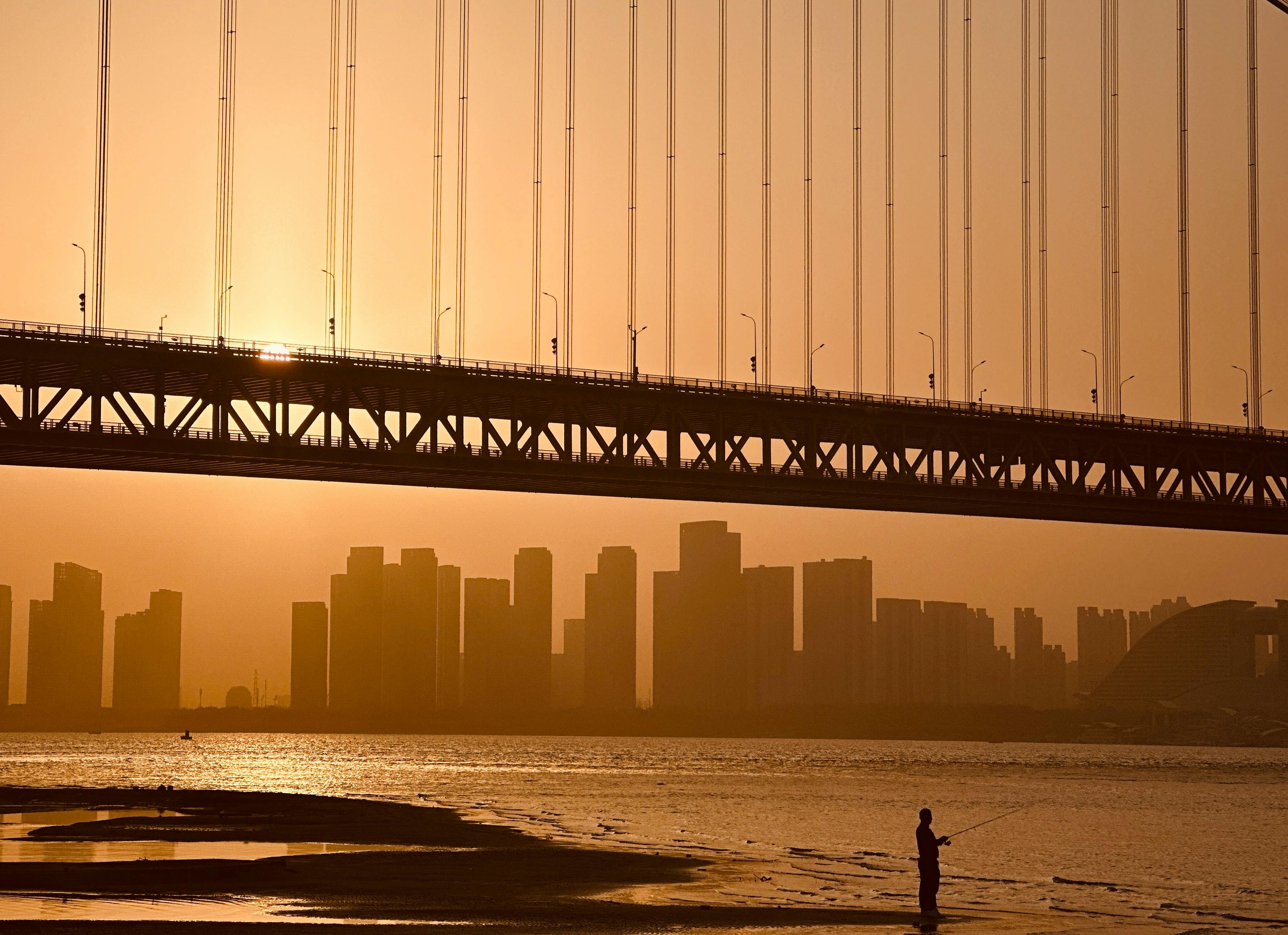 Kostenlos Silhouette einer Brücke in Wuhan, China, bei Sonnenuntergang mit der Skyline im Hintergrund. Stock-Foto