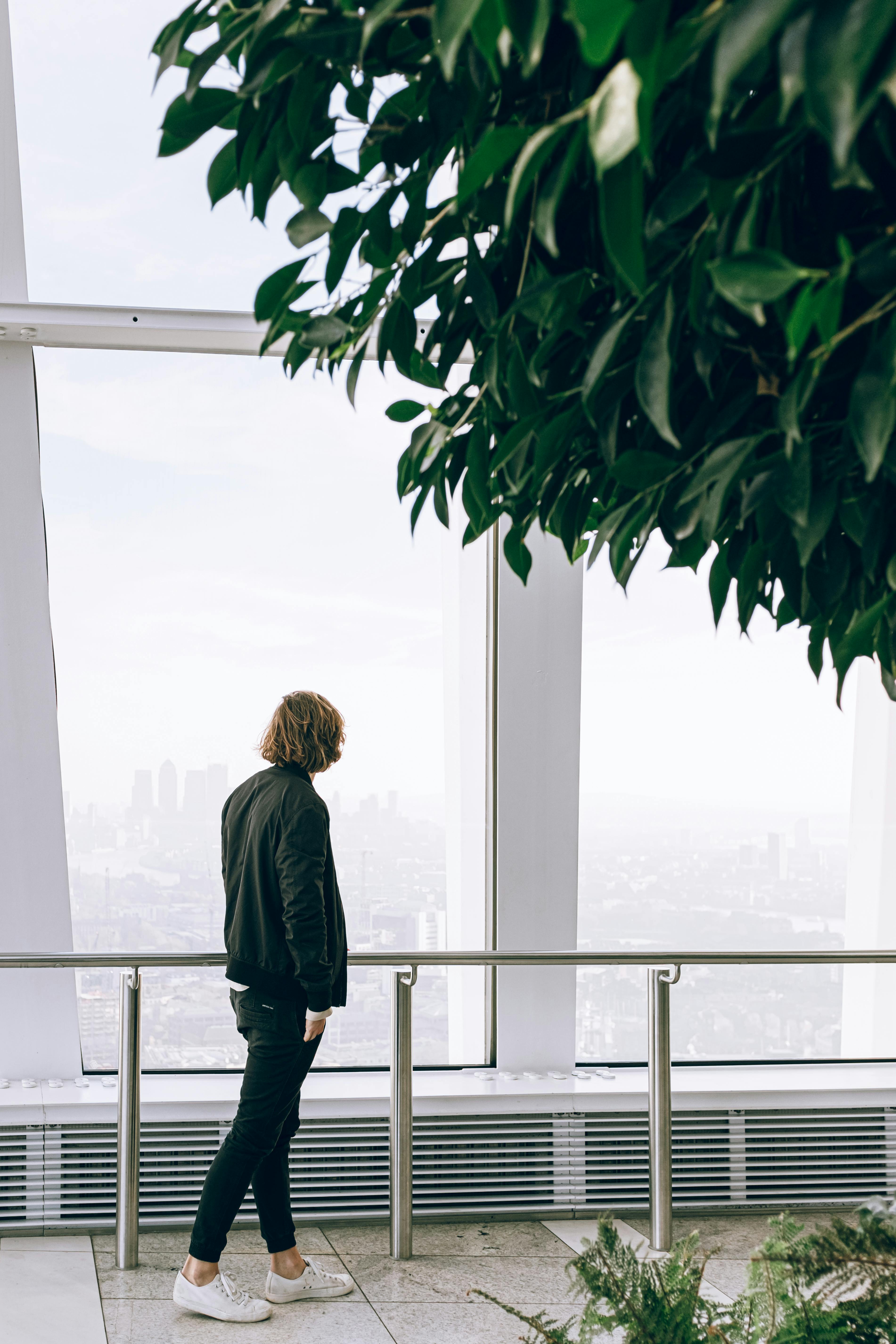 Man in Black Jacket Looking Out a Large Window