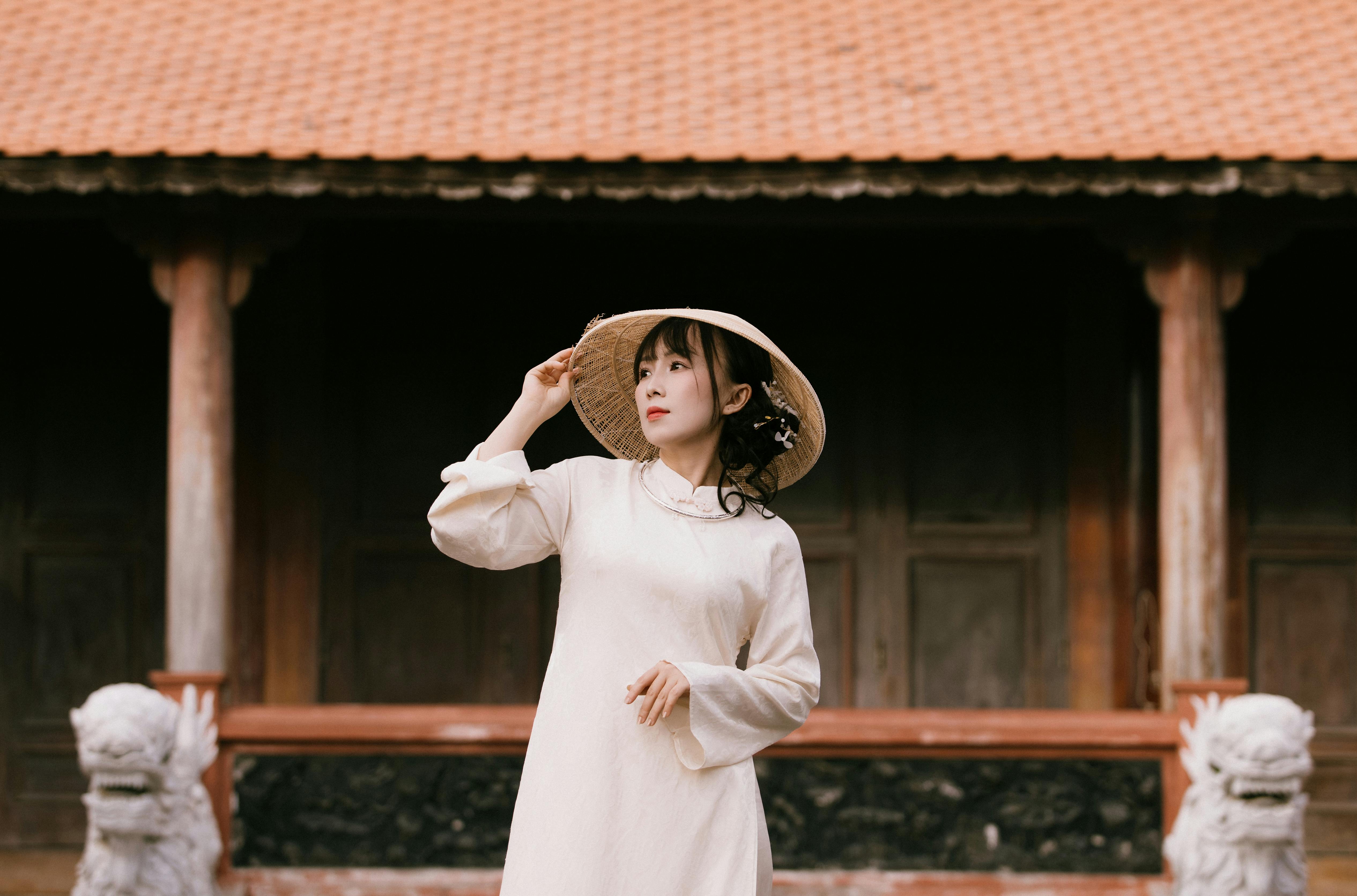Kostenlos Elegante Frau in traditioneller Kleidung und mit Kegelhut steht vor einem historischen Gebäude. Stock-Foto