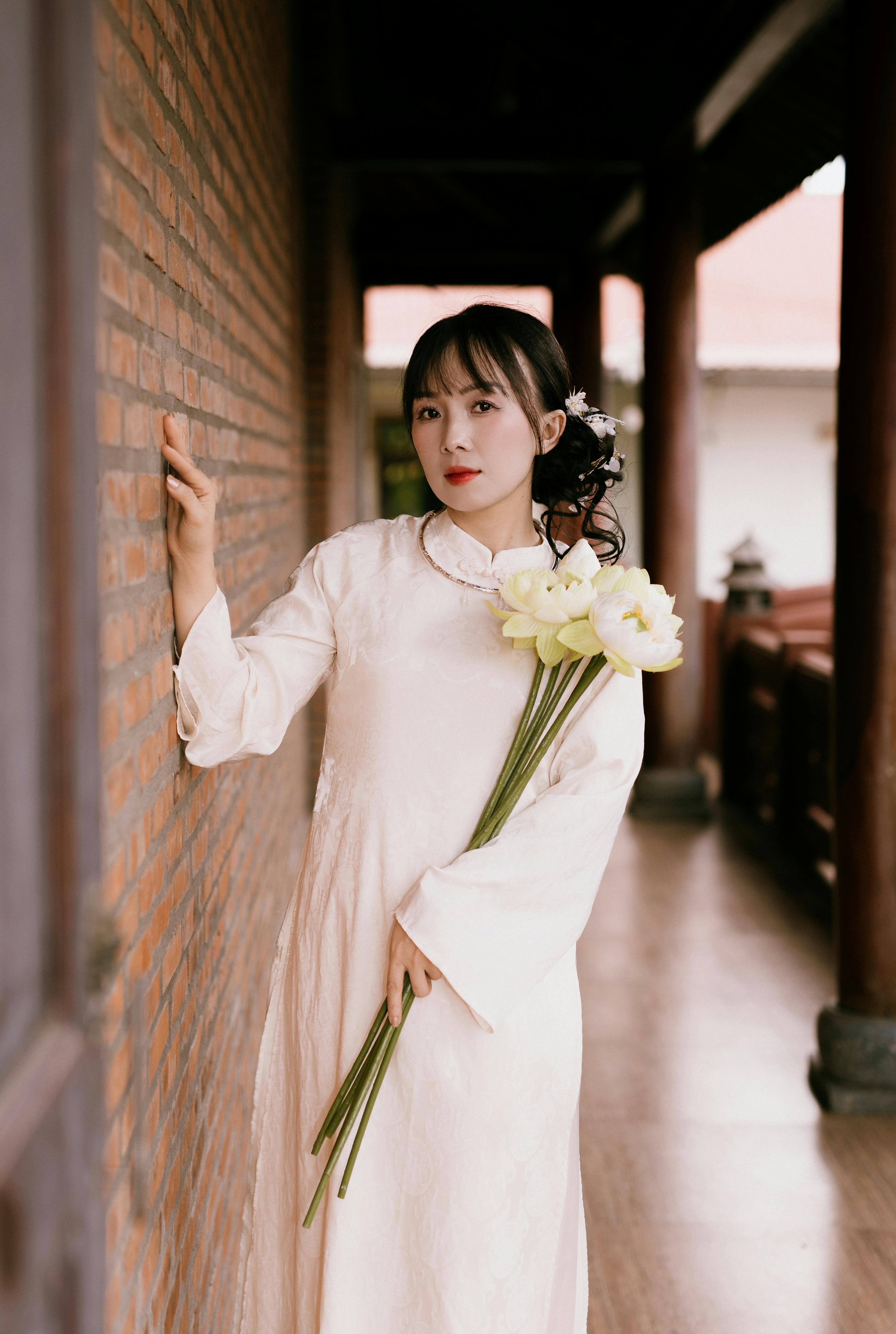 Kostenlos Eine Frau in traditioneller Kleidung posiert mit weißen Blumen in einem ruhigen Korridor. Stock-Foto