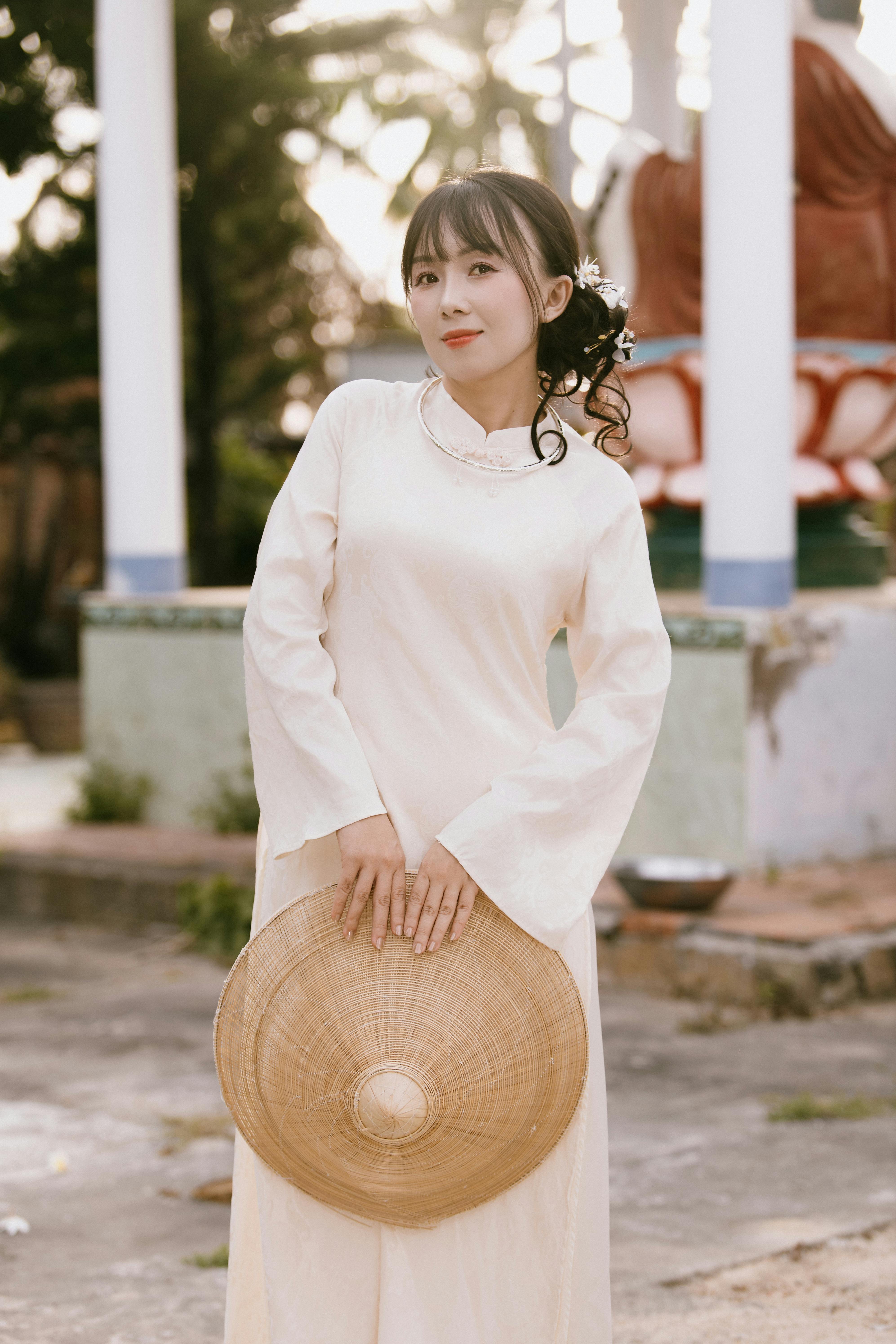 Kostenlos Eine Frau in traditioneller Kleidung, die einen Strohhut hält, steht im Freien. Stock-Foto