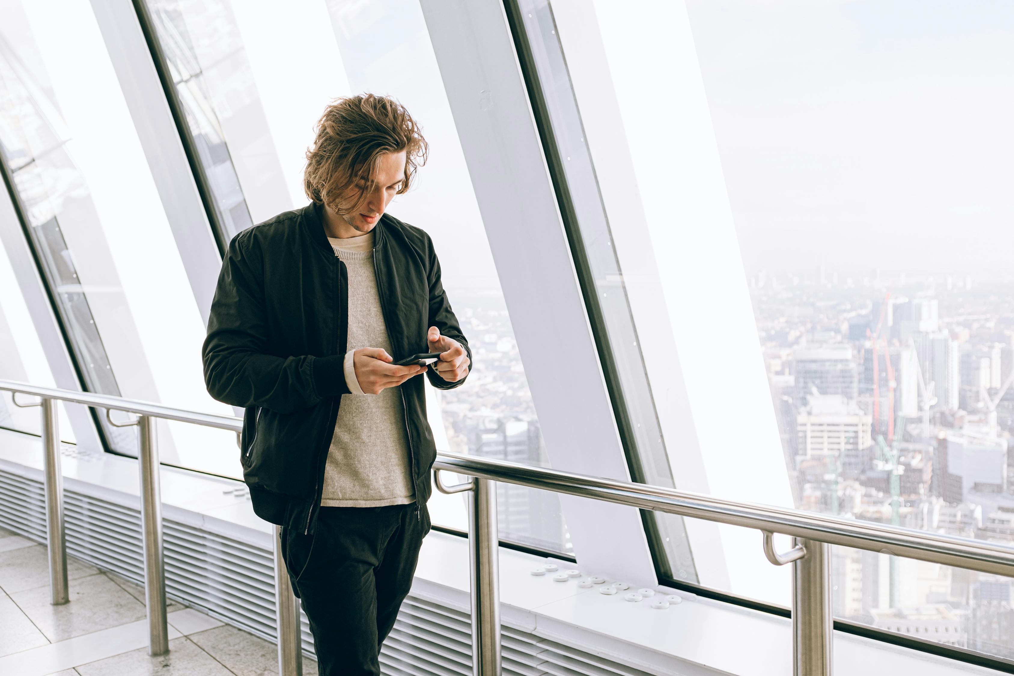 Man in Black Jacket Walking Beside Large Window