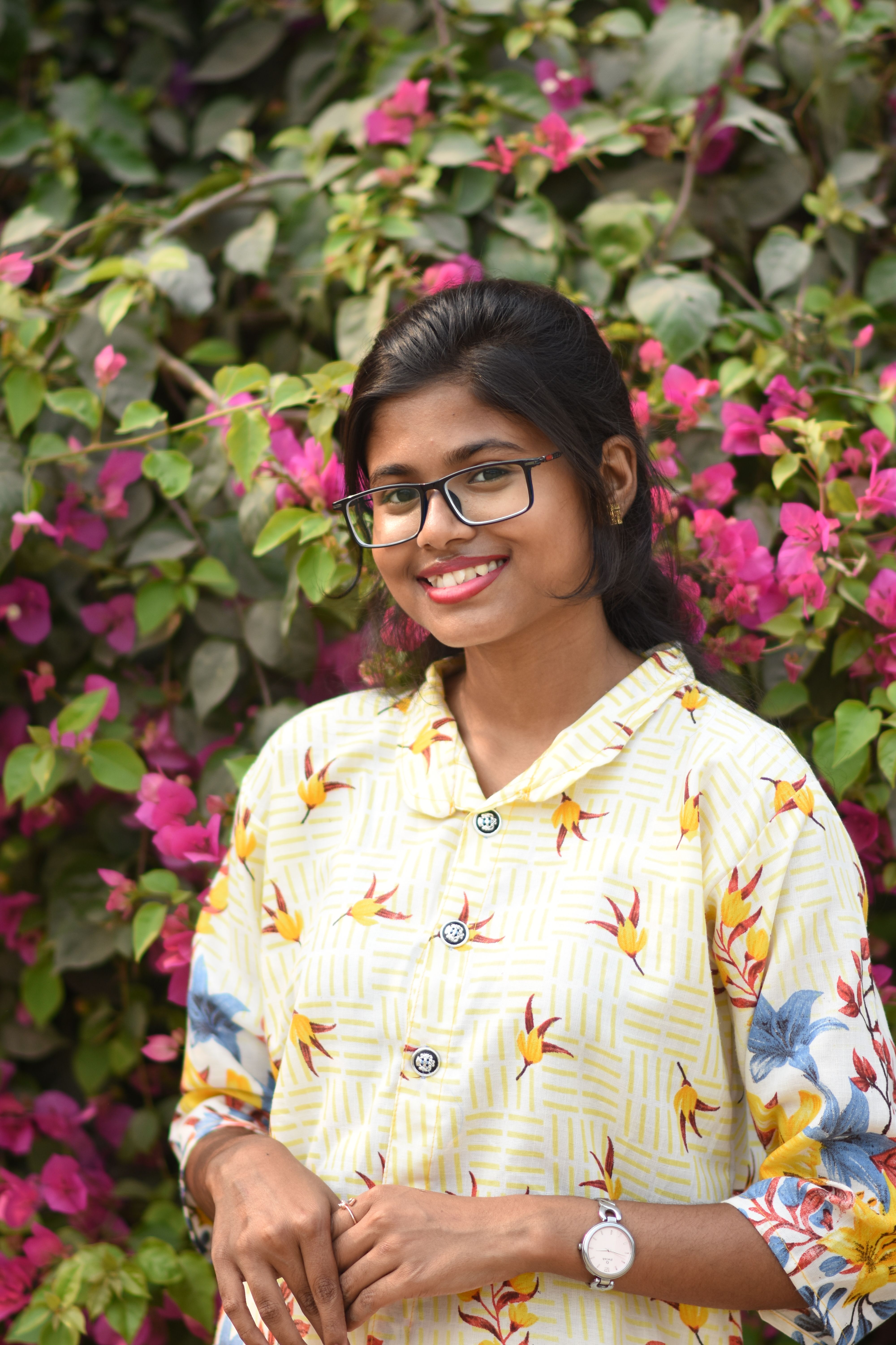 A South Asian woman smiling outdoors against a vibrant pink floral background in Kolkata.