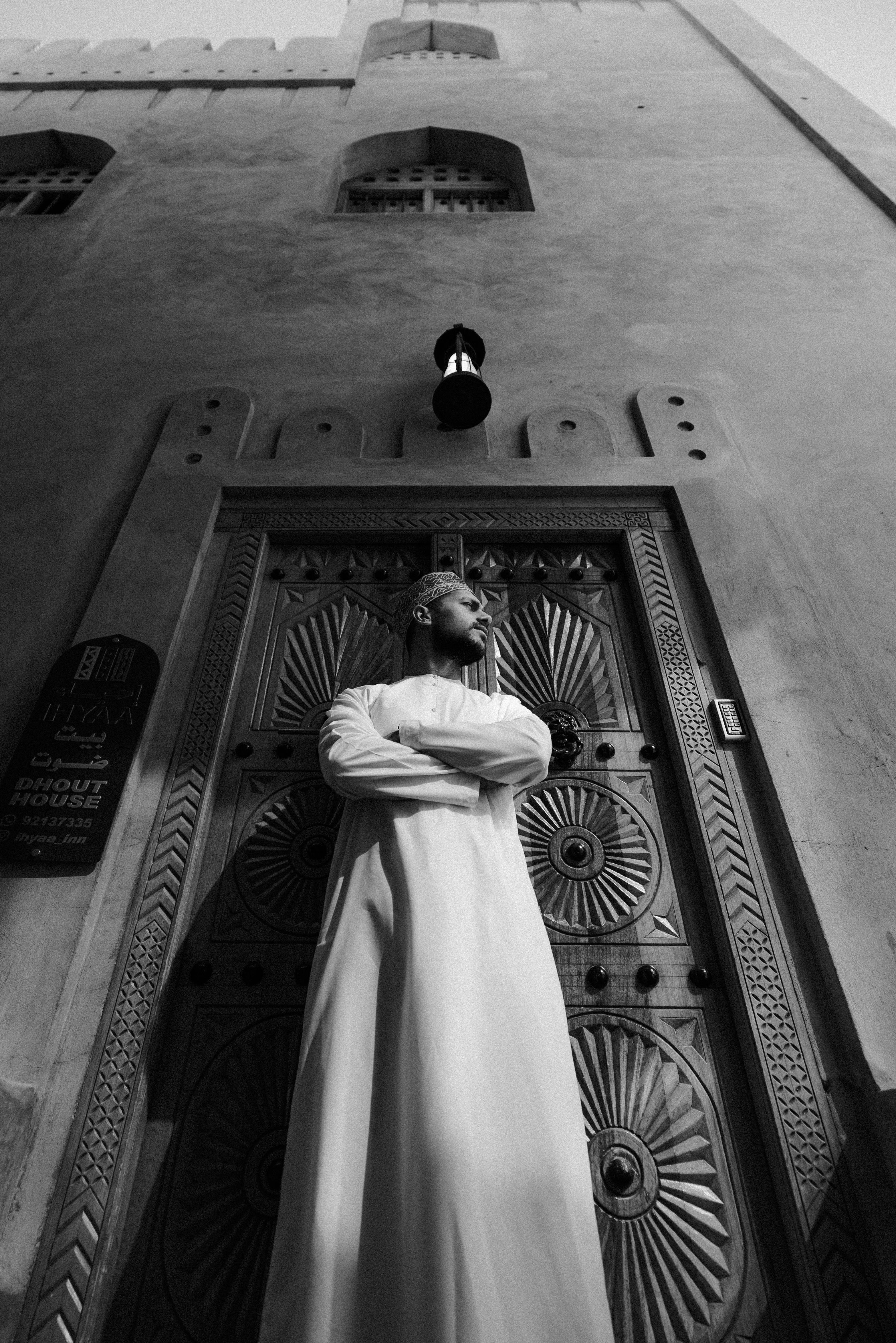 Δωρεάν Ασπρόμαυρο πορτρέτο ενός άνδρα με παραδοσιακή ενδυμασία που στέκεται με αυτοπεποίθηση δίπλα σε μια διακοσμητική πόρτα στο Ομάν. Φωτογραφία από στοκ φωτογραφιών