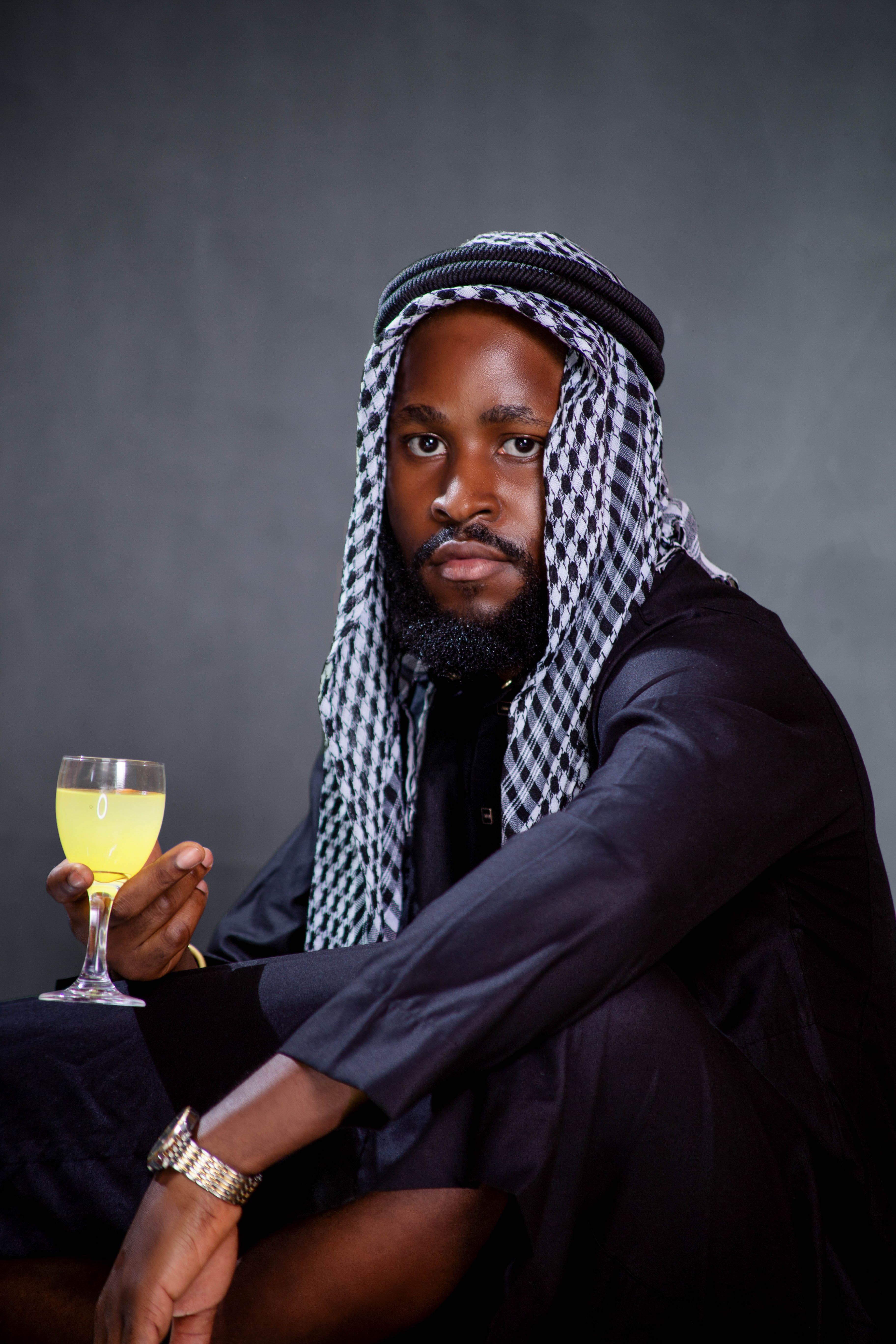 Man in traditional Middle Eastern clothing holding a glass of juice against a dark background.