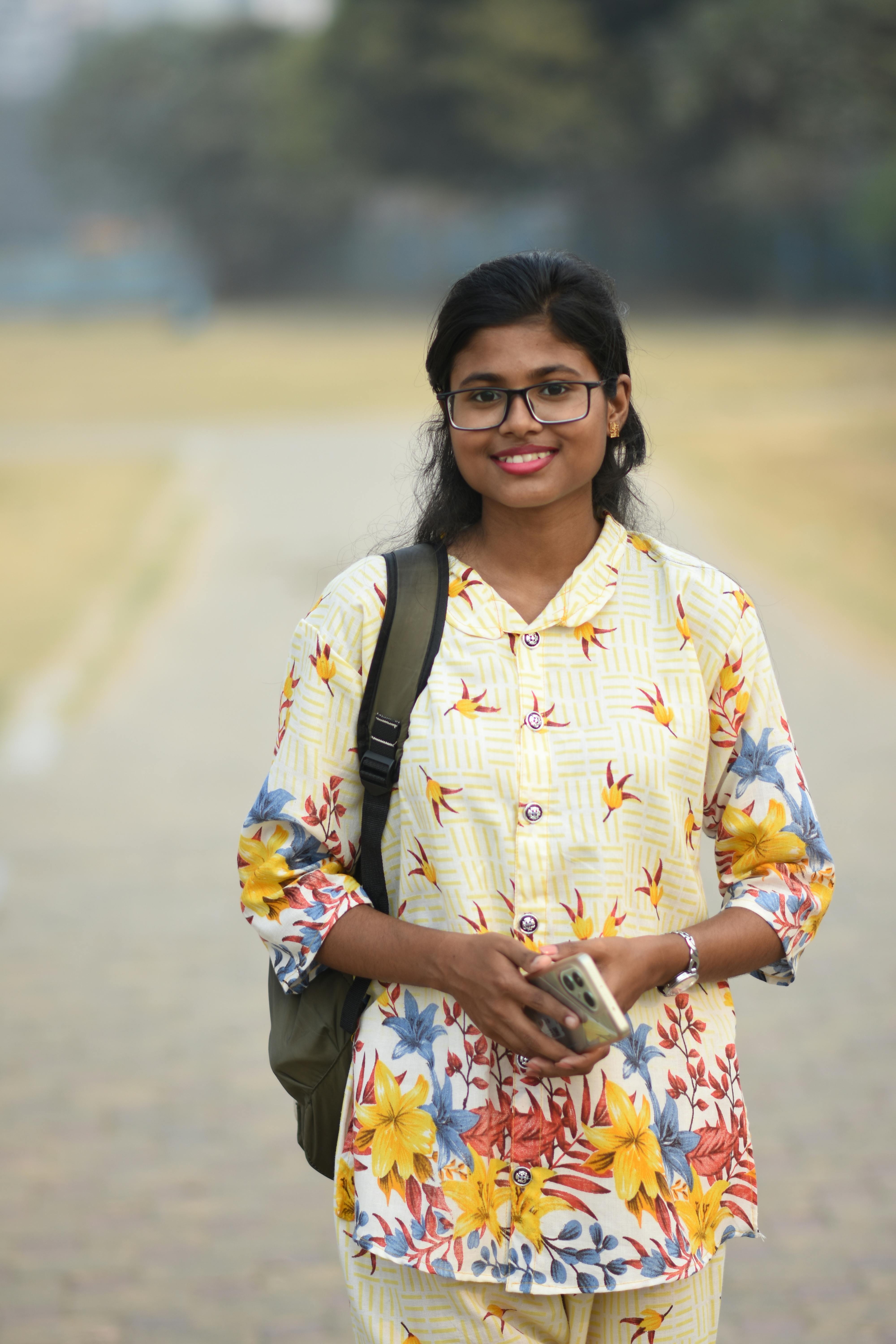 Cheerful young woman with glasses holding phone outdoors in Kolkata, India.