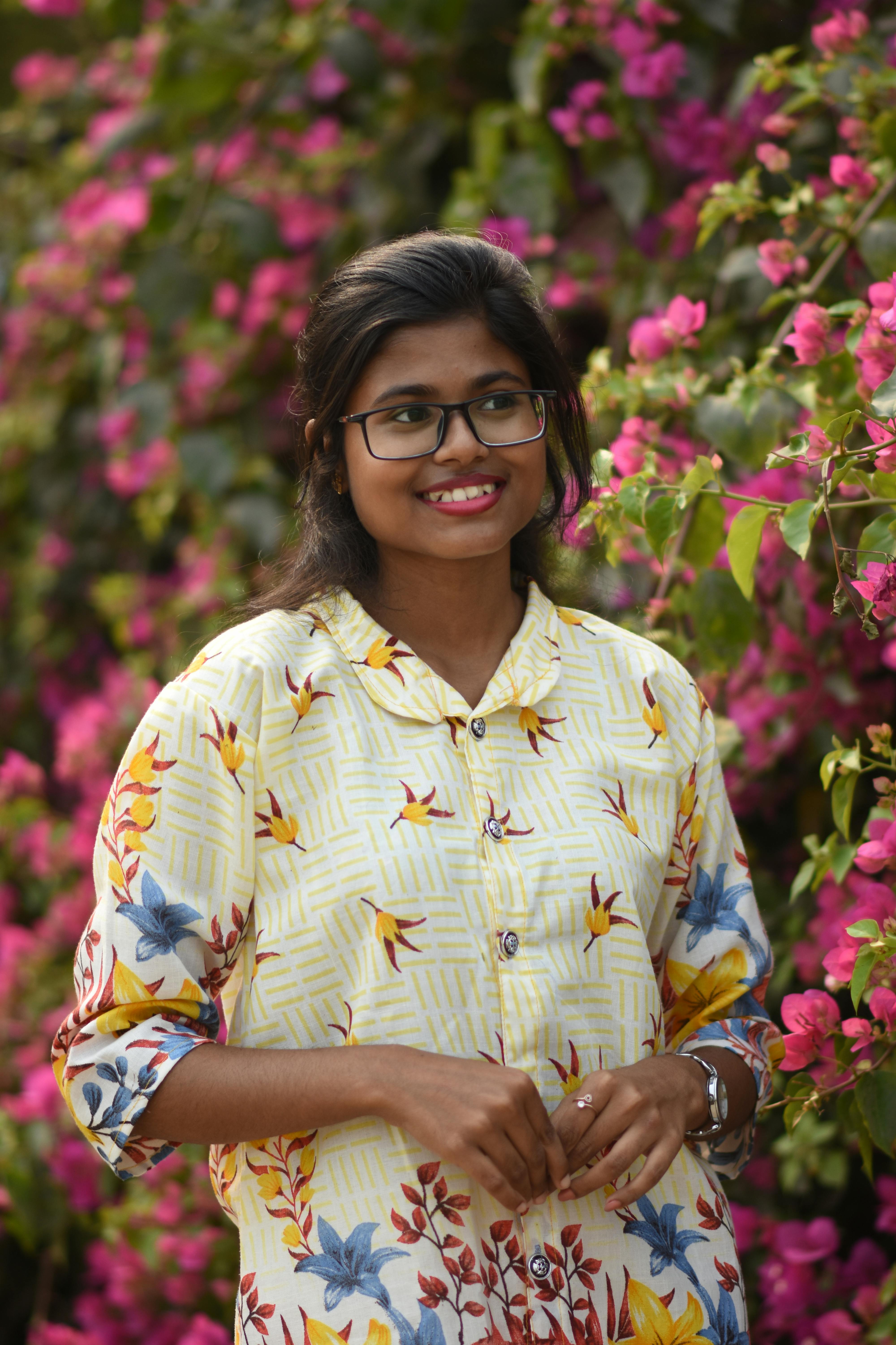 Portrait of a young woman in a floral dress standing amidst colorful flowers in Kolkata, India.