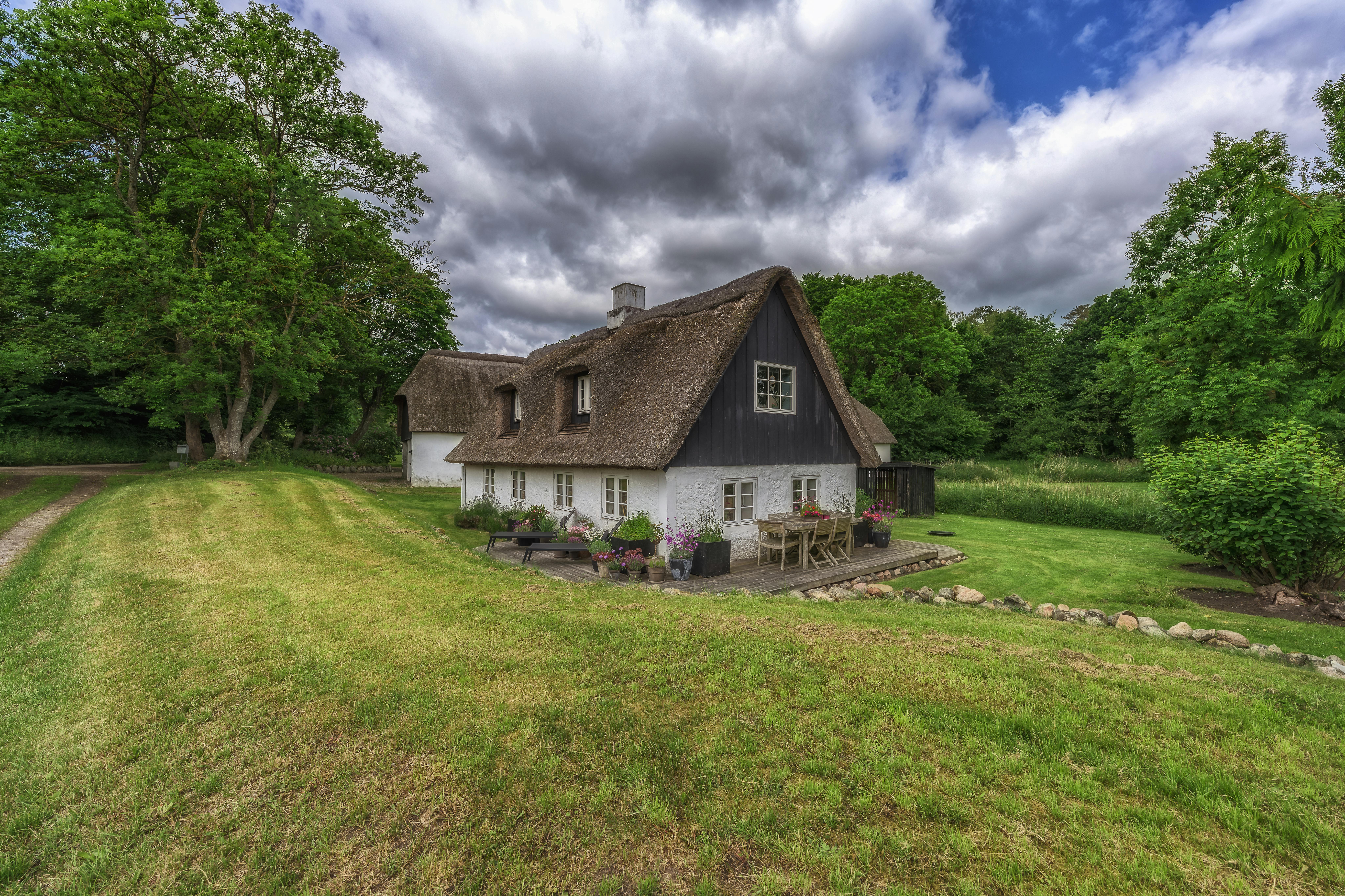 Un pittoresque chalet au toit de chaume à Aarhus, au Danemark, entouré d'une végétation luxuriante et de nuages ​​ondulants.