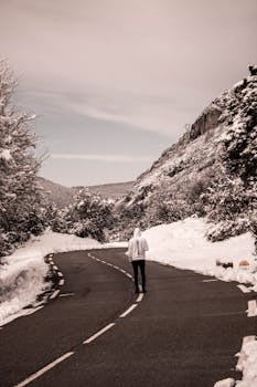 A person walks alone on a snow-covered mountain road, capturing winter's quiet solitude.