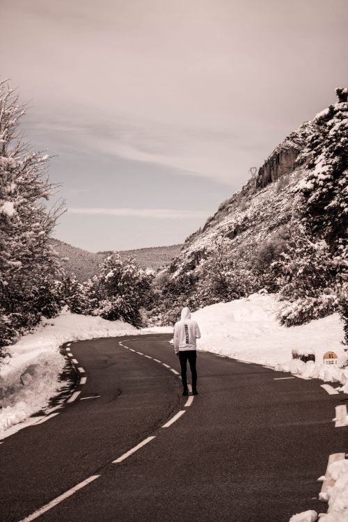 Free A person walks alone on a snow-covered mountain road, capturing winter's quiet solitude. Stock Photo