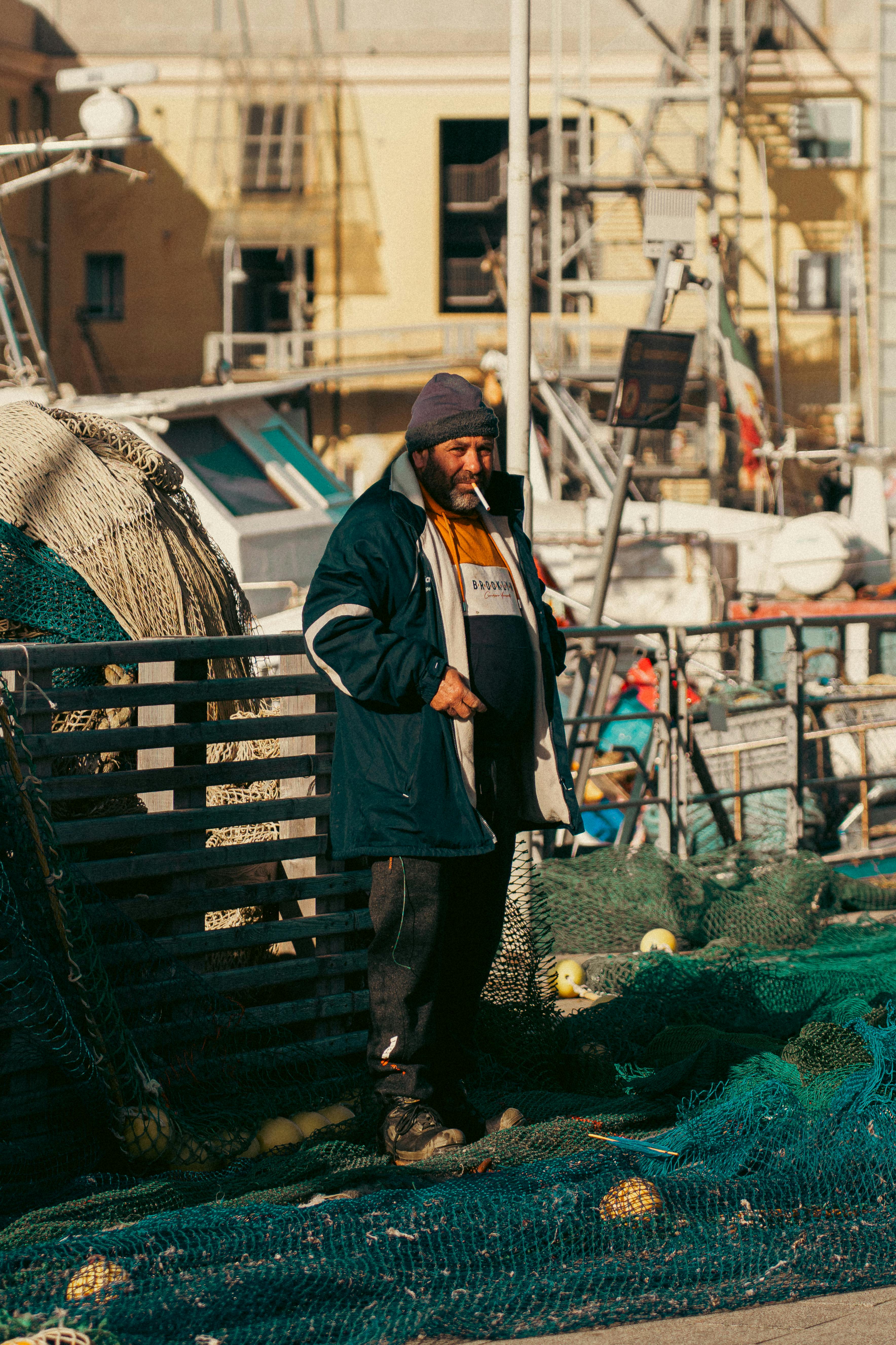 Δωρεάν Ένας ψαράς στέκεται ανάμεσα σε δίχτυα στο πολύβουο λιμάνι της Γένοβας, στη Λιγουρία της Ιταλίας. Φωτογραφία από στοκ φωτογραφιών