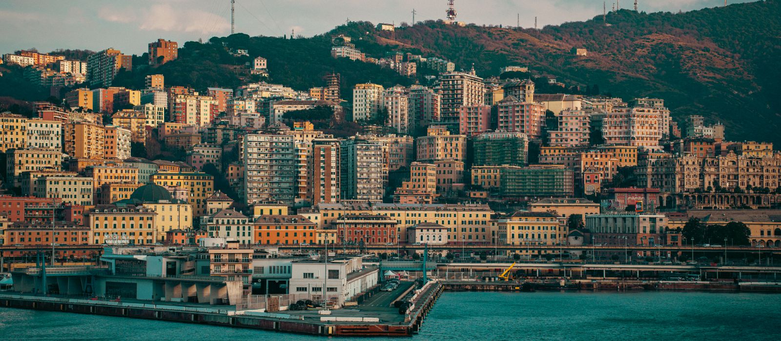 Scenic shot of Genoa's vibrant coastal skyline with colorful buildings against a hilly backdrop.