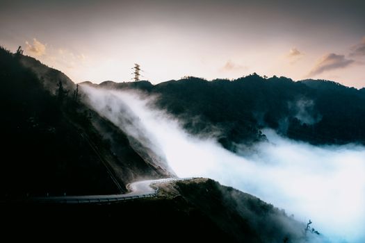 Dramatic view of a winding road through misty mountains at sunrise, capturing nature's beauty.